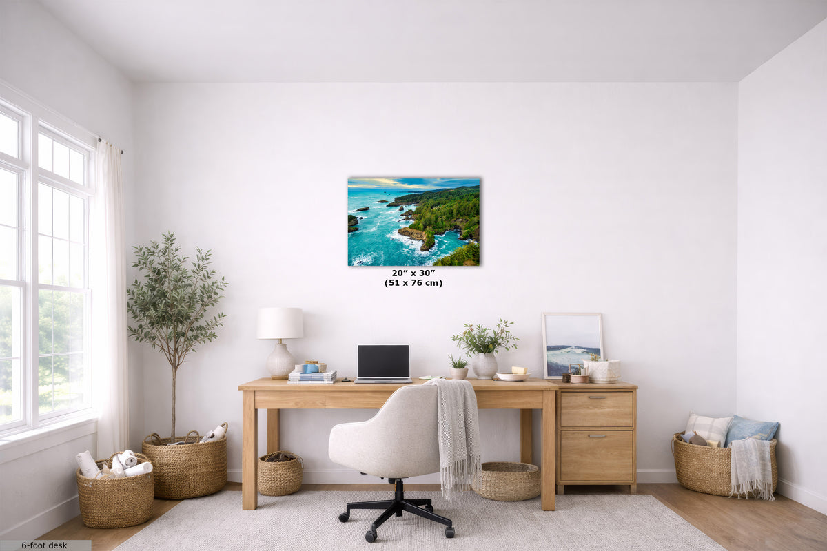 A 20" x 30" canvas print of a coastal landscape with turquoise water and green cliffs, displayed on a white wall above a wooden desk in a bright, modern home office.