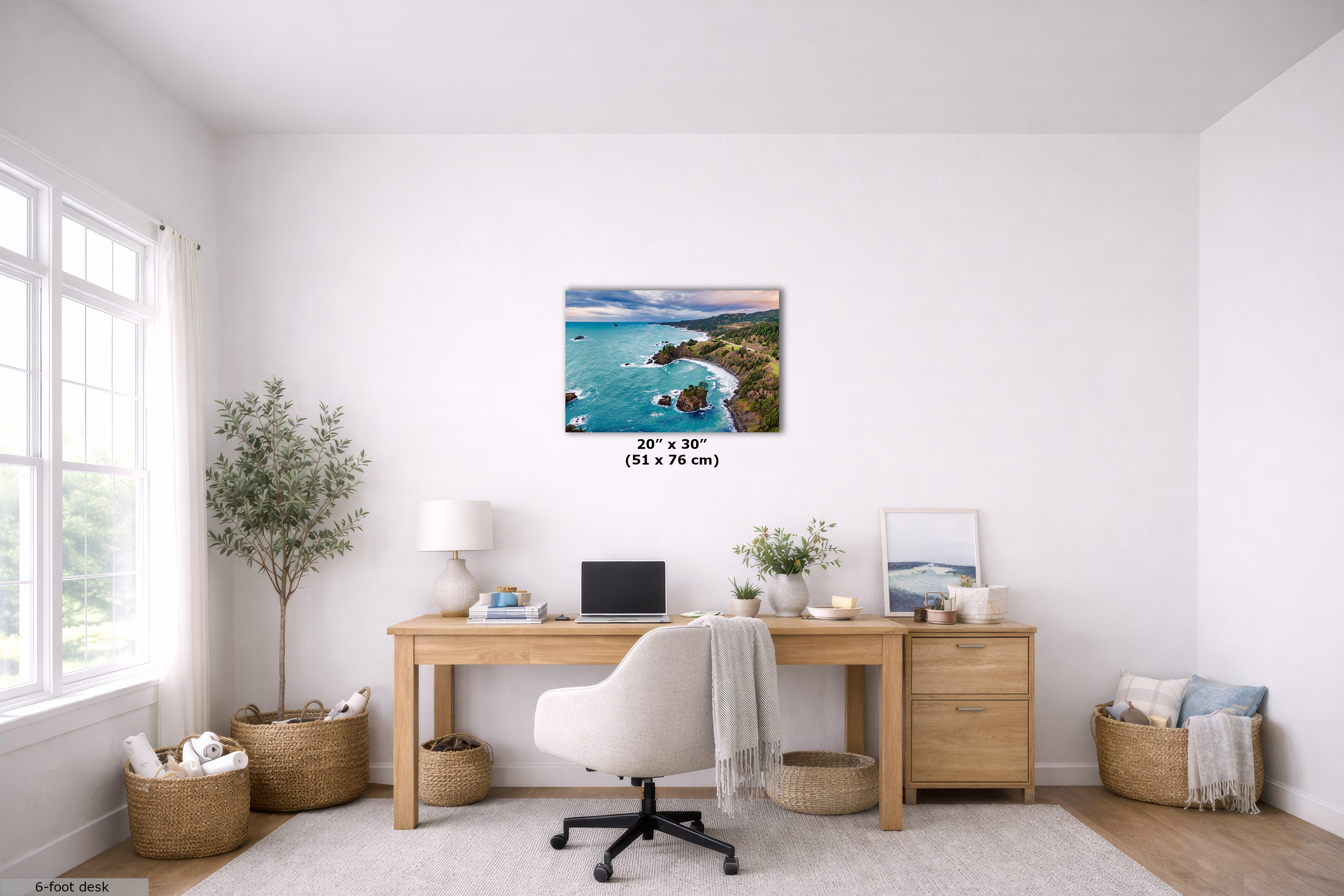 A 20" x 30" square canvas print of a coastal rocky shoreline with turquoise water, displayed on a white wall in a bright, modern home office setting above a wooden desk.