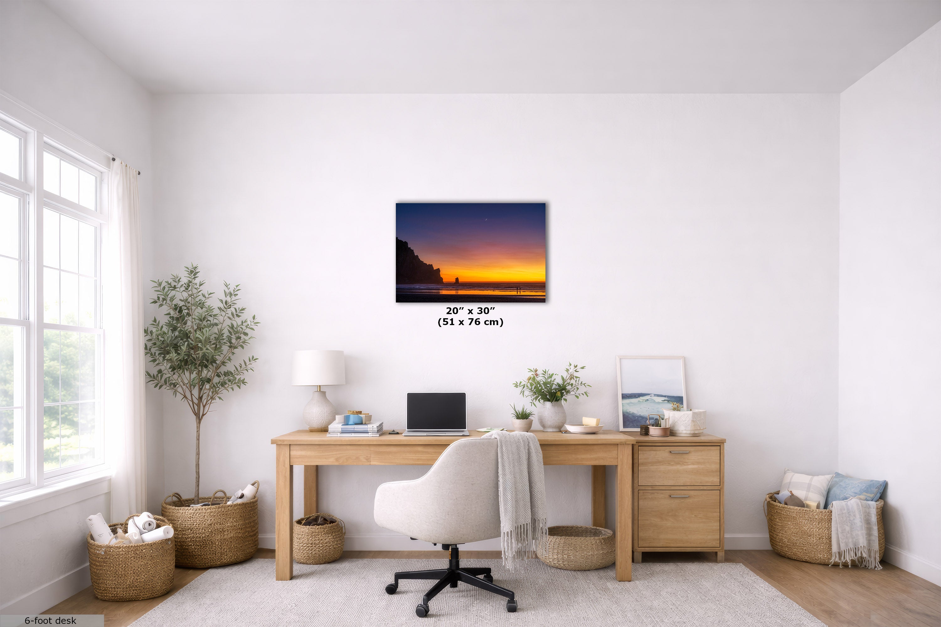 A wall art print showing a sunset over a cliff is displayed in a bright, modern home office setting above a wooden desk with a white office chair. The print has a black frame and size text overlay indicating 20" x 30" (51 x 76 cm).