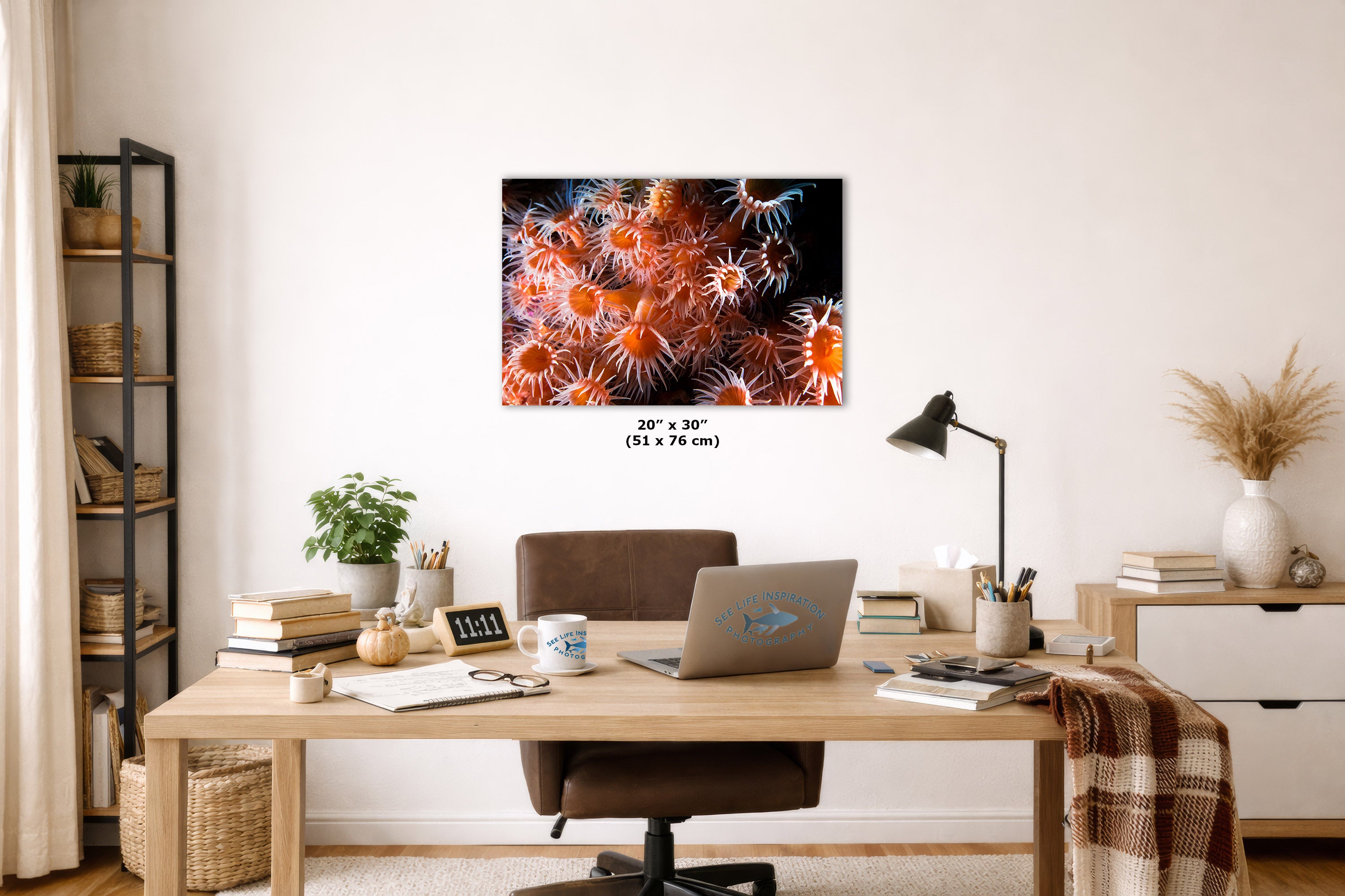 A wall art print depicting a close-up of orange and red sea anemones on a black background, styled in a modern home office setting above a wooden desk.