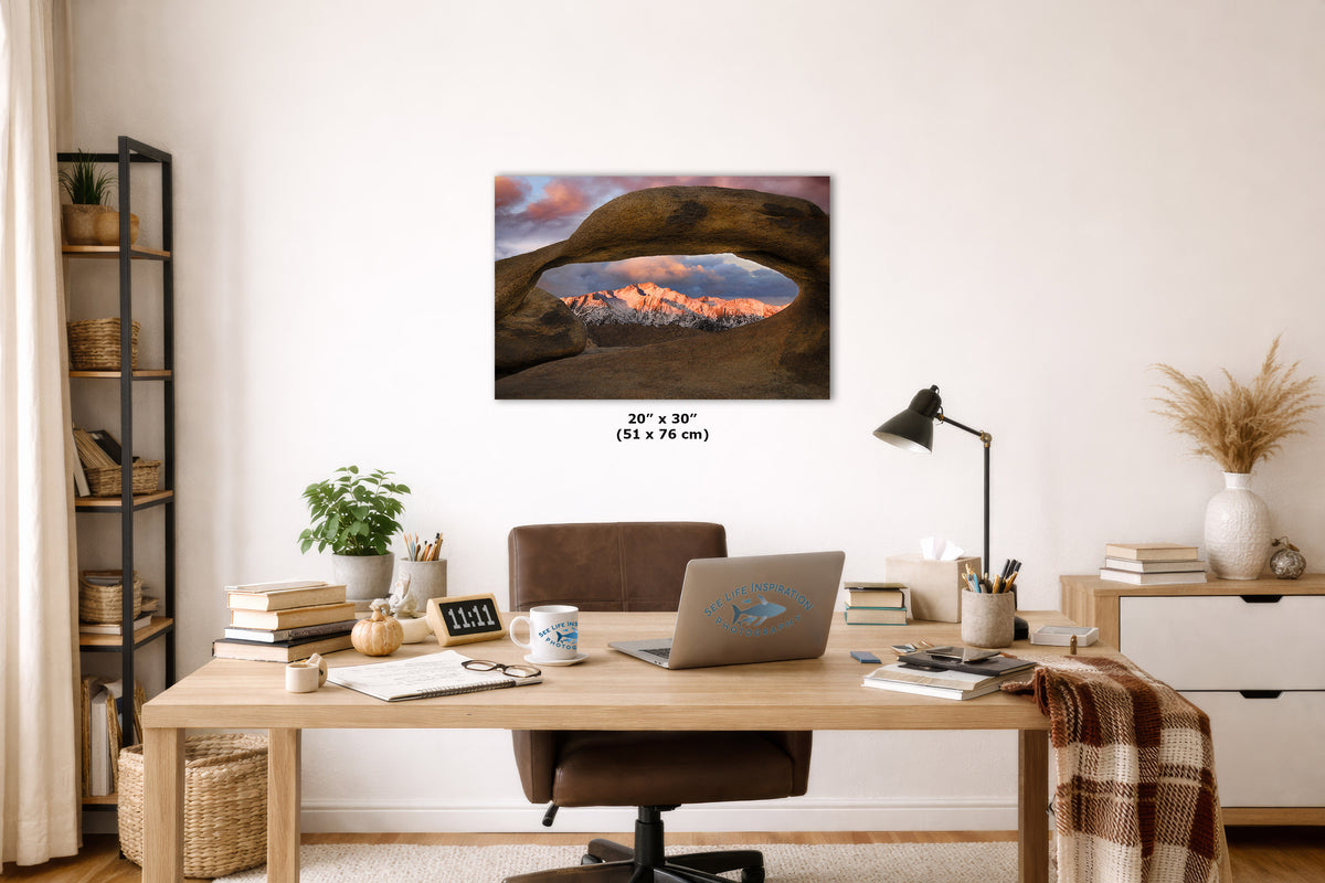 A wall art print looking through a desert arch to Lone Pine peak at sunrise, displayed above a wooden desk in a styled home office setting.