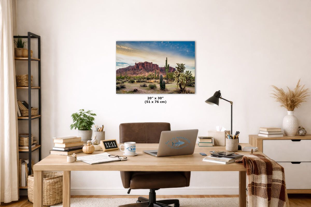 A wall art print depicting a desert landscape with red rock formations and cacti, displayed above a wooden desk in a styled home office setting. The print includes size text reading 20 x 30" (51 x 76 cm) below it.