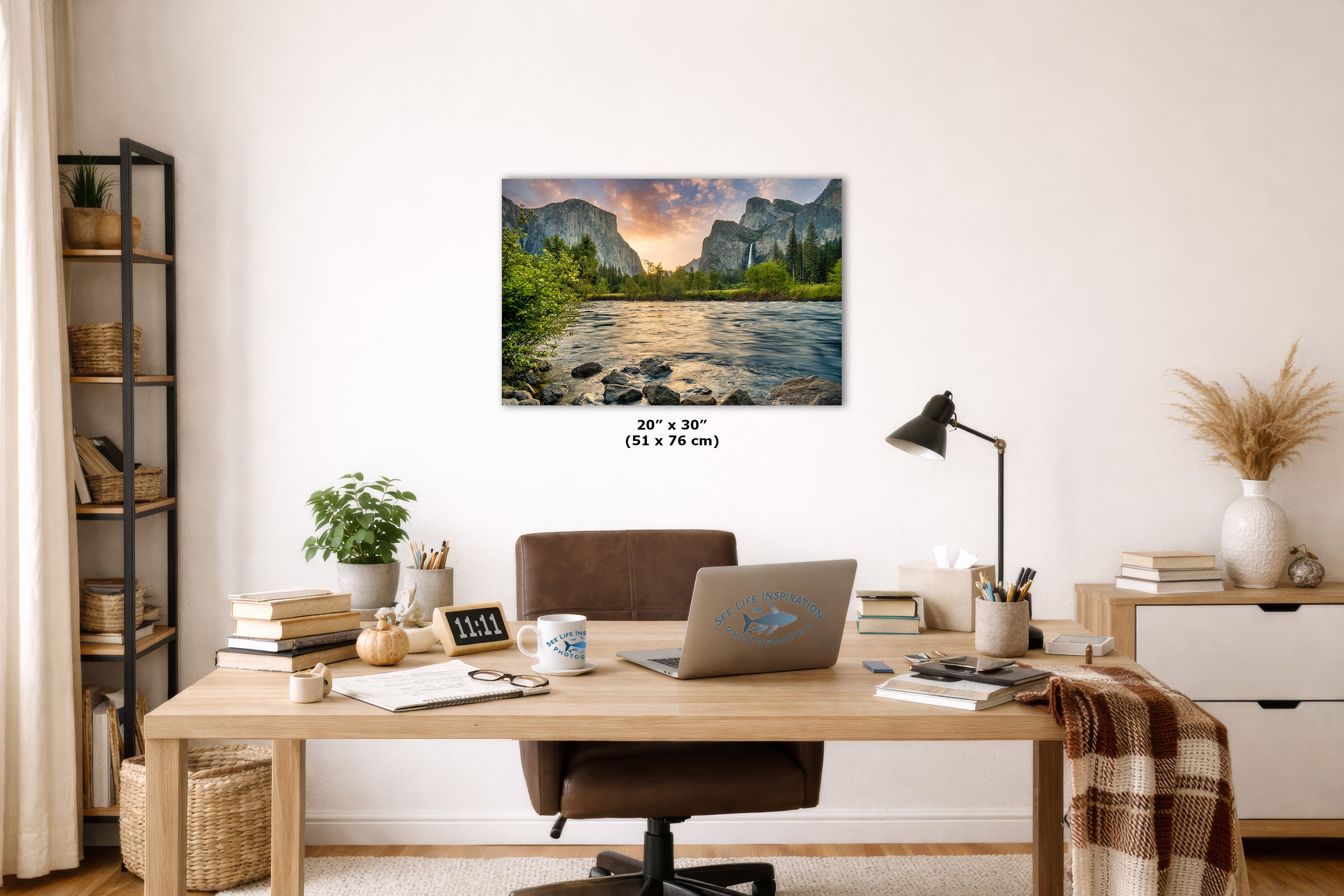 A framed wall art print showing a mountain river landscape with a sunset sky, displayed above a wooden desk in a styled home office interior. The print includes size text reading 20" x 30" (51 x 76 cm) below it.