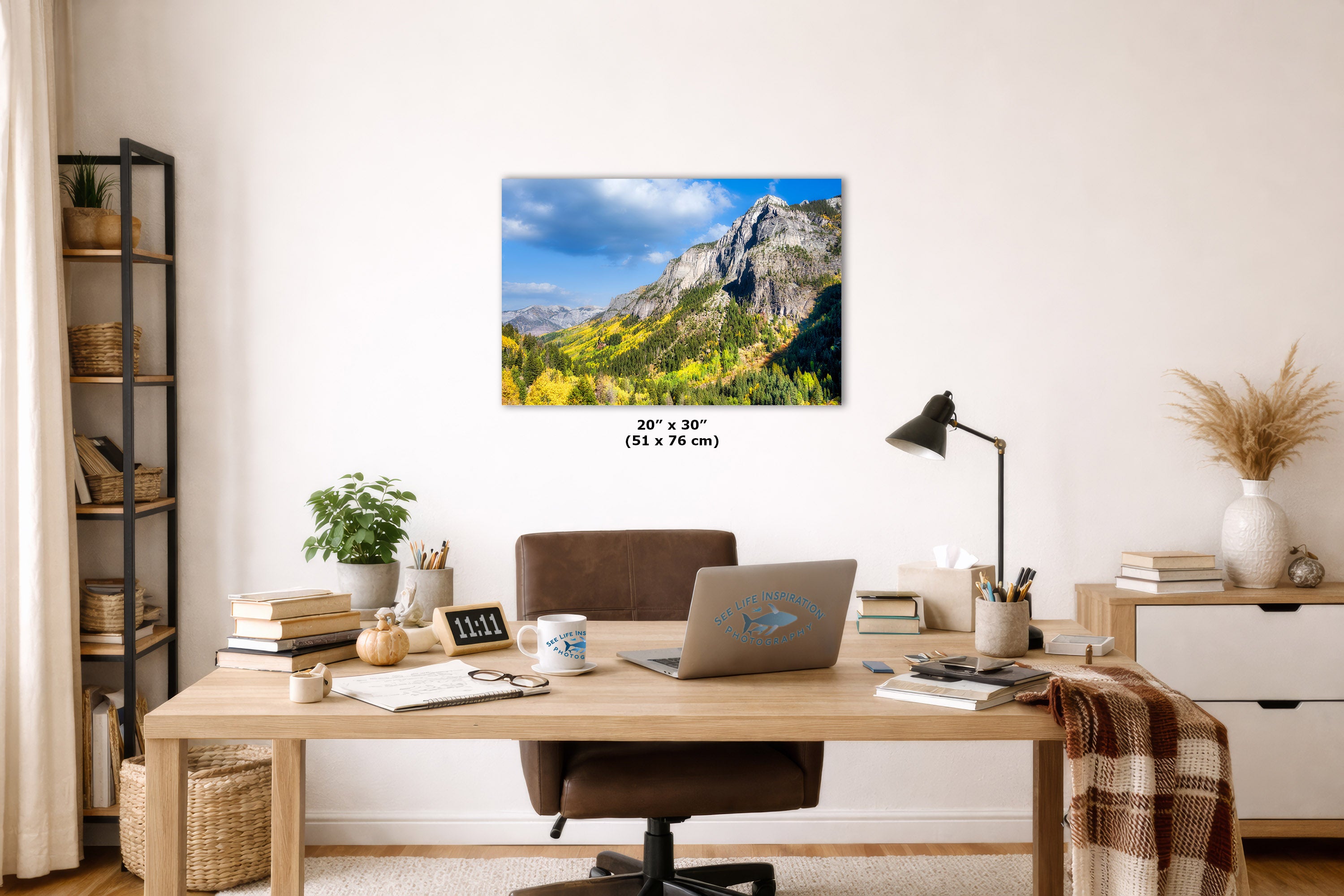 Home office with a desk, laptop, and decorative items, featuring a large wall-mounted picture of a mountain landscape.