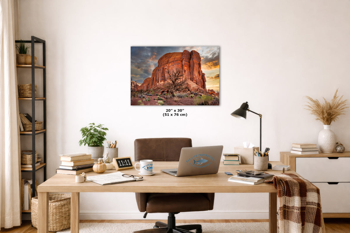 A wall art print depicting a desert rock formation at sunset hangs above a wooden desk in a styled home office. The print is shown as the product, with the room serving as a lifestyle context.