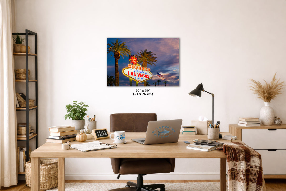 A wall art print depicting the Las Vegas sign at dusk hangs above a wooden desk in a styled home office. The print shows palm trees, a colorful sky, and the iconic sign, with size text centered below it.