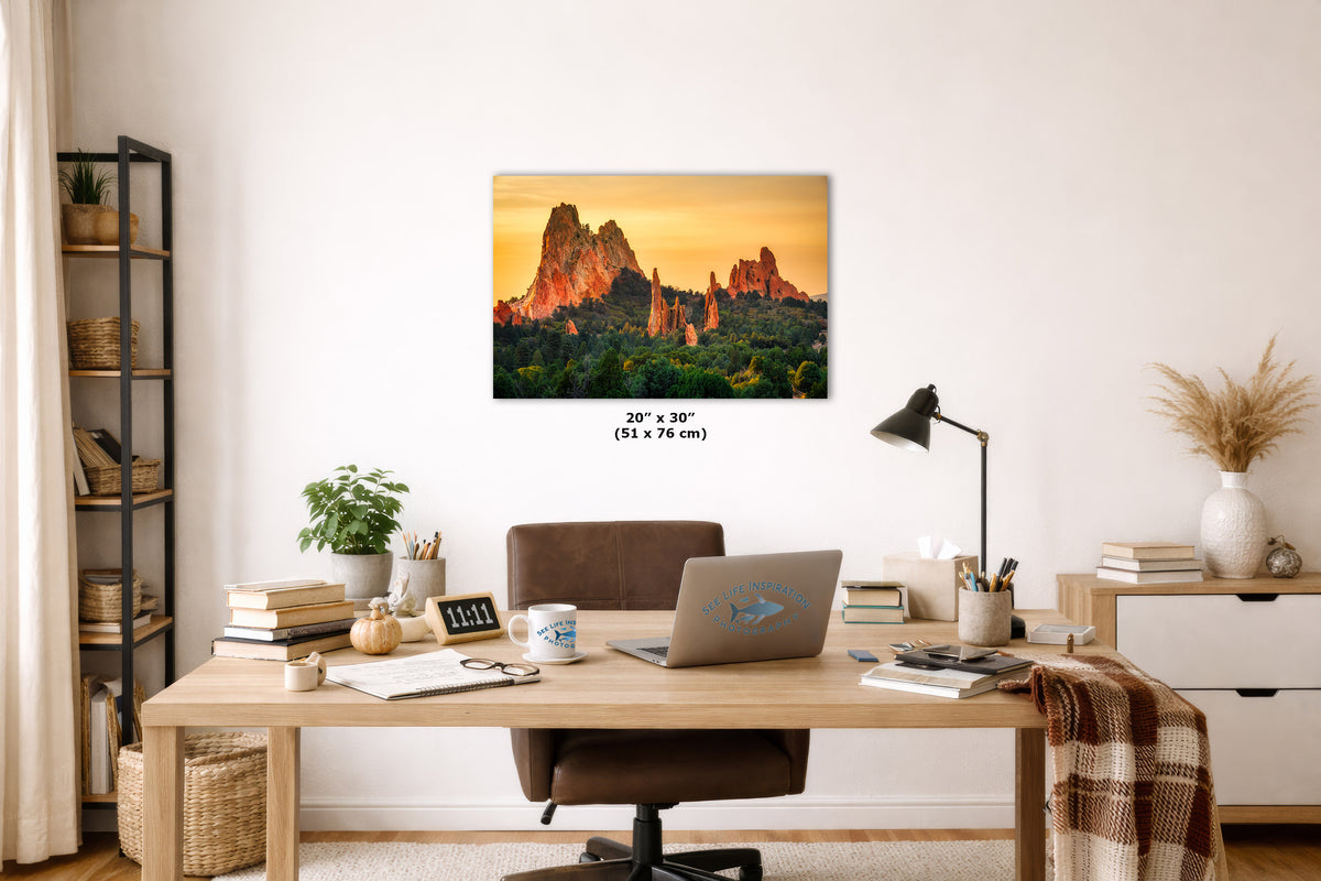 A wall art print showing a warm sunset landscape with tall rock formations hangs above a wooden desk in a styled home office. The print includes size text reading 20 x 30 inches.