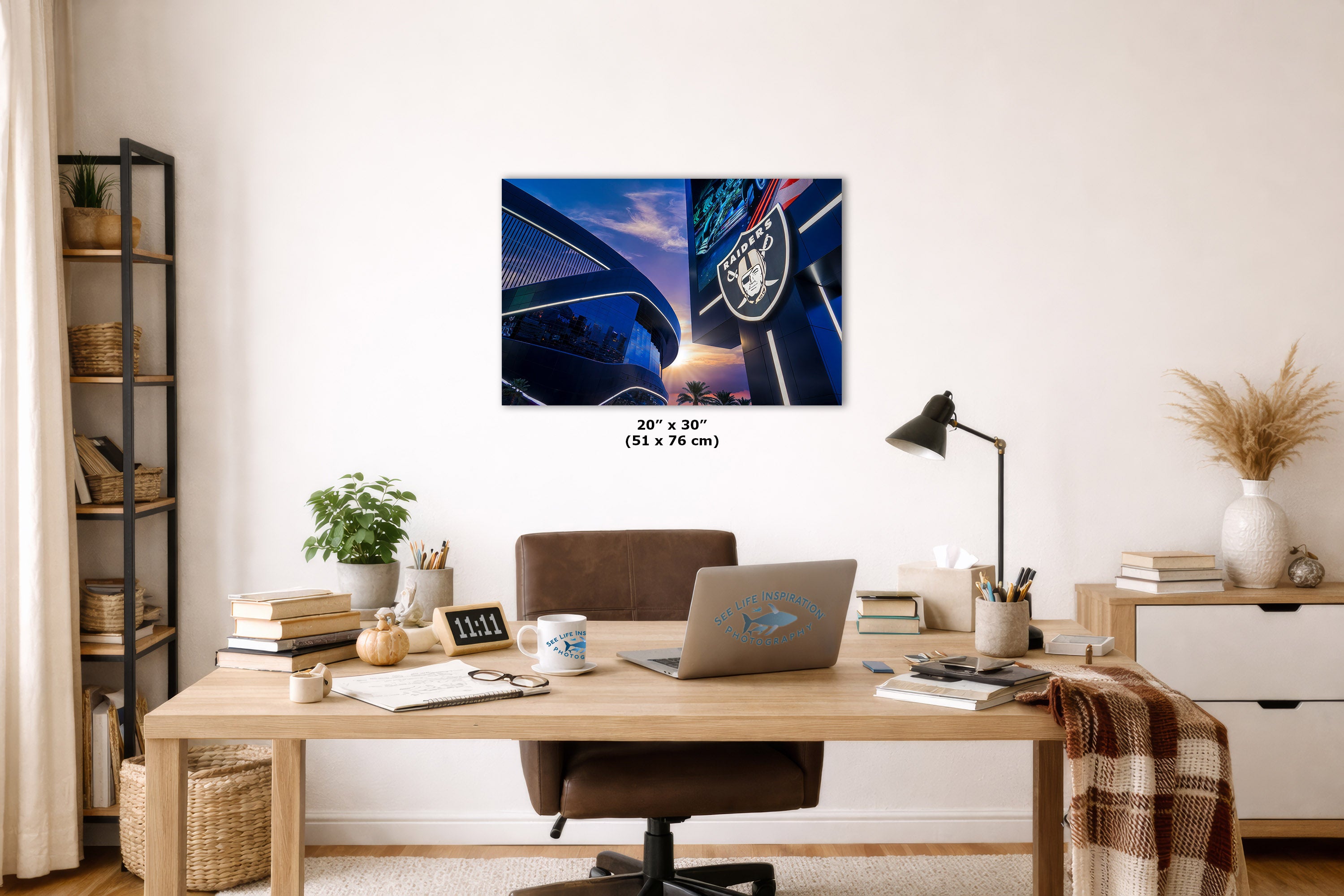 A wall art print showing a close-up of a blue car door and window with a sunset sky, displayed above a wooden desk in a styled home office. The print includes size text reading 20" x 30" (51 x 76 cm) and features a small visible brand mark on the artwork.