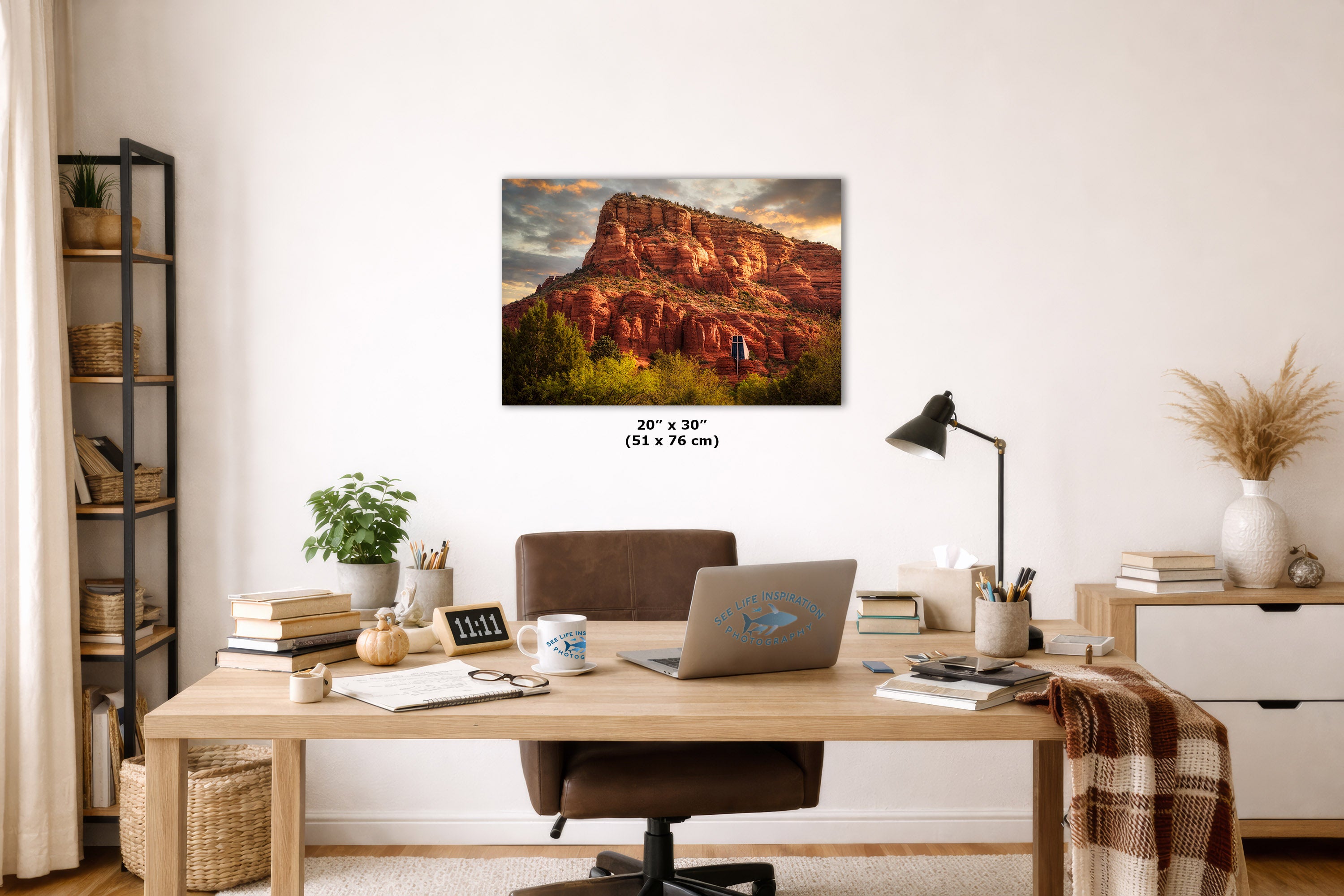 A wall art print depicting a red rock desert canyon at sunset hangs above a wooden desk in a styled home office. The print is shown as the product within a real interior setting, so this is Lifestyle rather than Product/Packaging.
