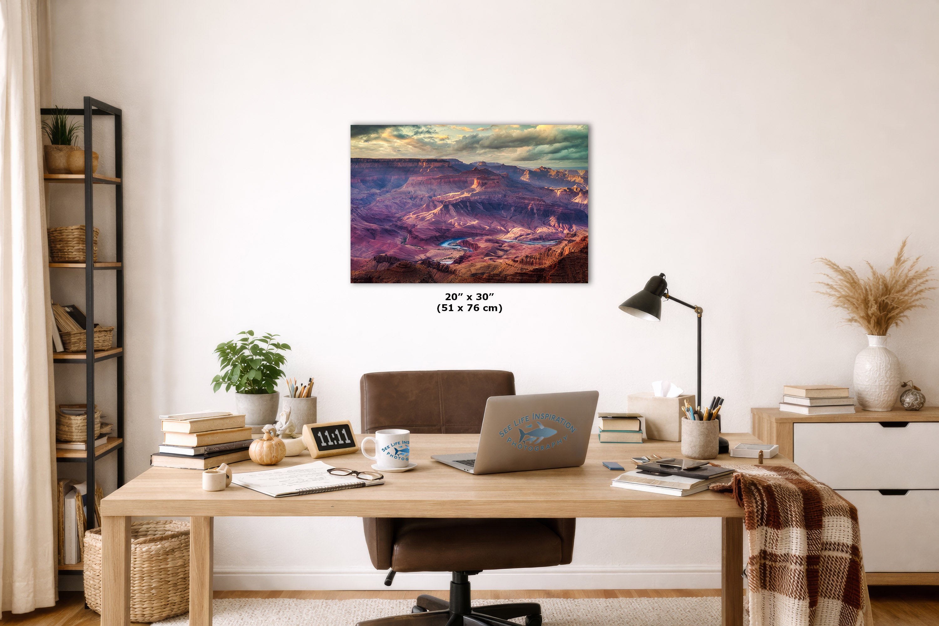 A colorful landscape art print of the Grand Canyon hangs on a white wall in a styled home office setting. The print features a vibrant, multicolored canyon scene with purple, blue, green, and orange tones.