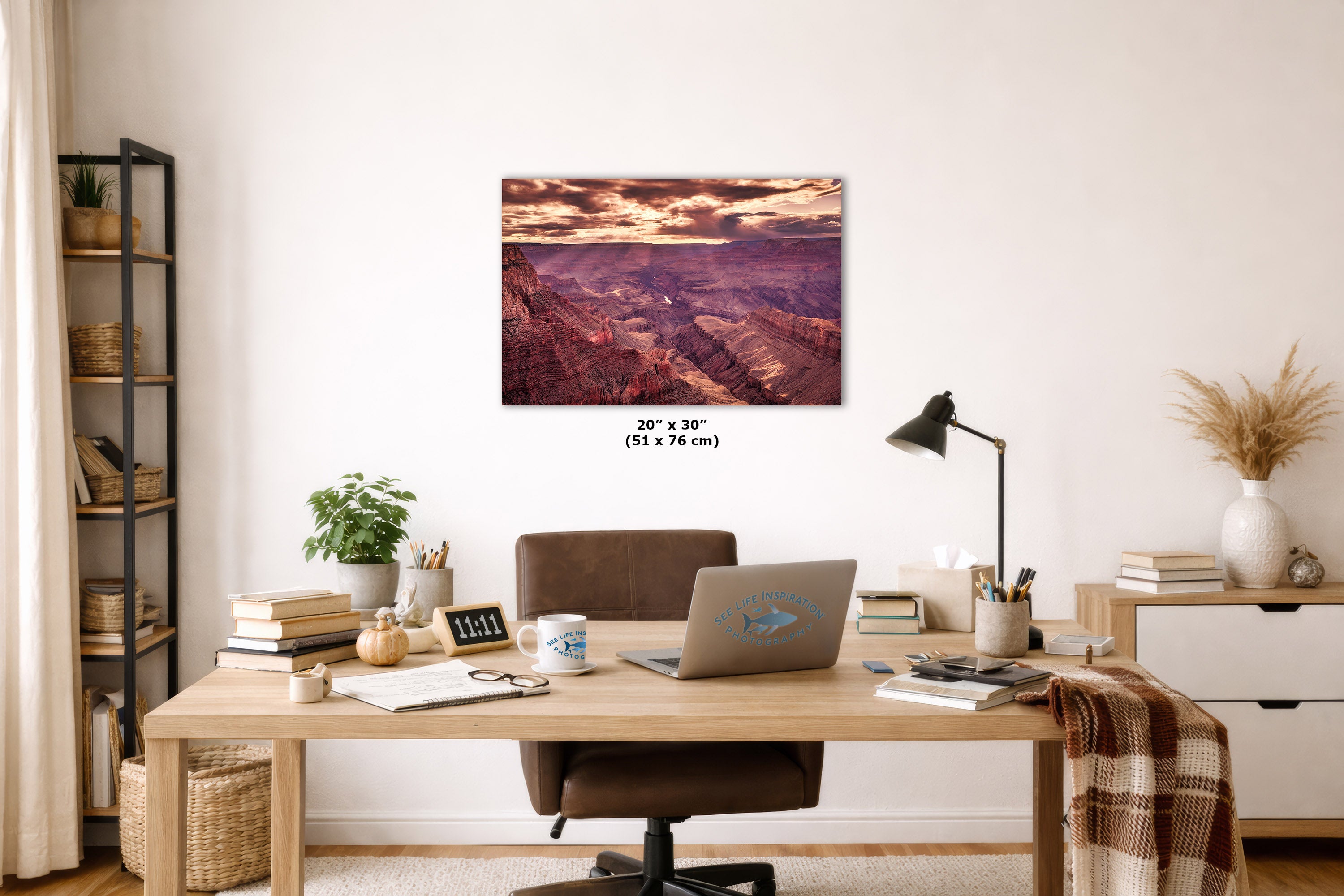 A wall art print depicting a scenic canyon landscape with warm sunset tones, displayed above a wooden desk in a styled home office setting. The print includes size text reading 20 x 30 inches (51 x 76 cm) below it.