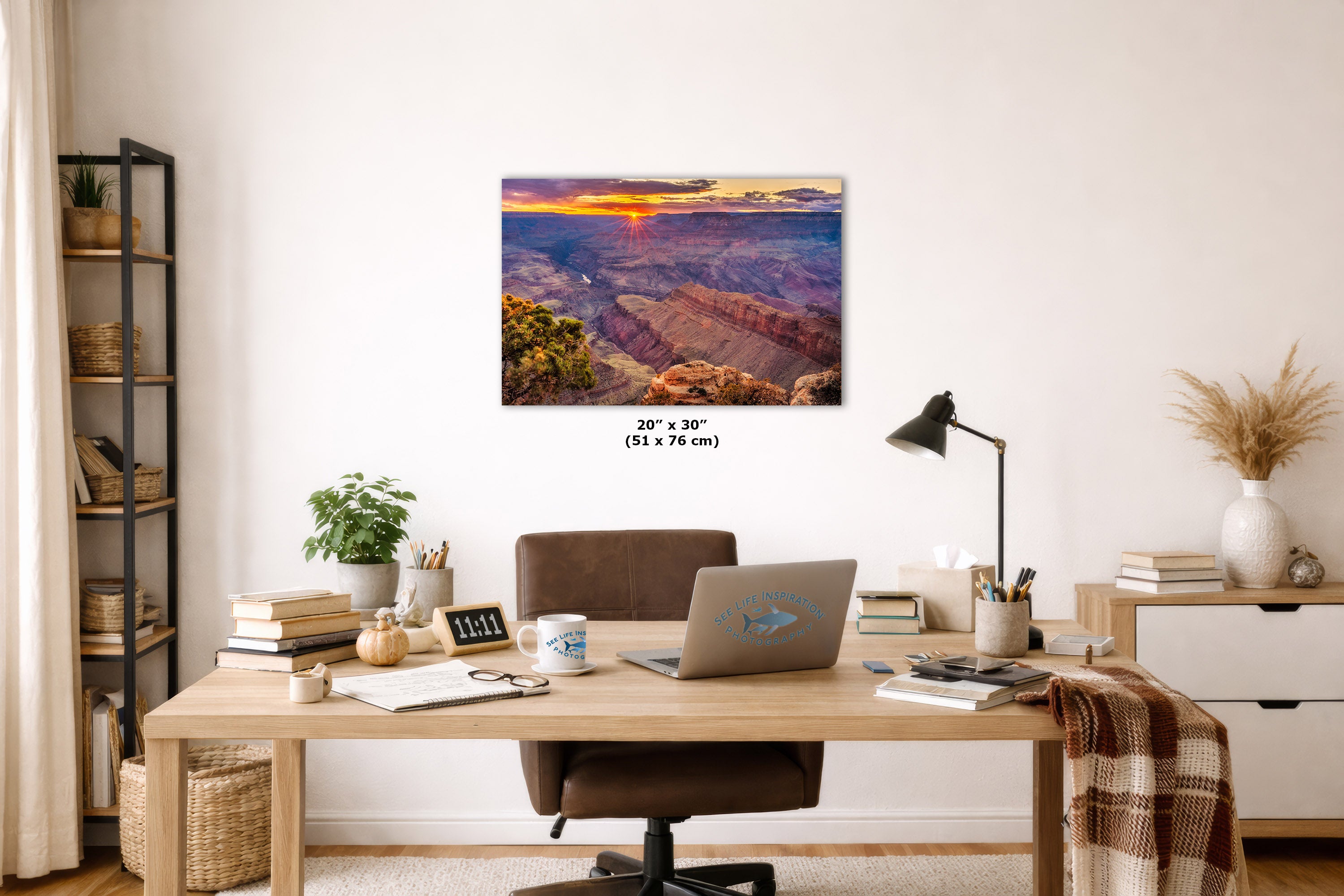 A rectangular wall art print showing a Grand Canyon sunset scene, displayed above a wooden desk in a styled home office. The print includes size text reading 20 x 30 inches.