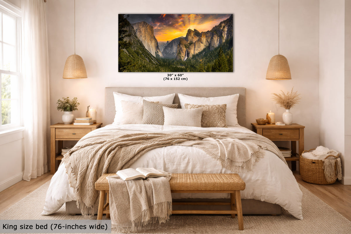 A framed wall art print showing a mountain landscape at sunset hangs above a neatly made bed in a bright, modern bedroom. The print includes size text reading 30 x 60 in (76 x 152 cm), and the room scene is styled with bedding, nightstands, lamps, and a bench.