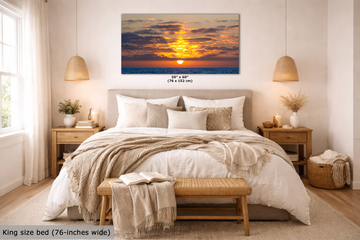 A framed wall art print showing a colorful sunset over the ocean, displayed above a neatly made bed in a modern, warm-toned bedroom. The print includes size text reading 30 x 60 inches (76 x 152 cm), and a text overlay at the bottom left says 'King size bed (76-inches wide)'.