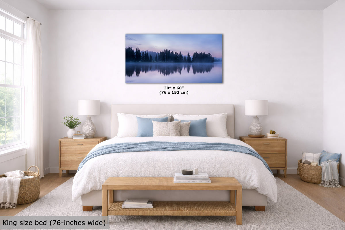 A bedroom mockup showing a framed wall art print above a bed. The print depicts a misty forest lake at dusk with blue, purple, and green tones.