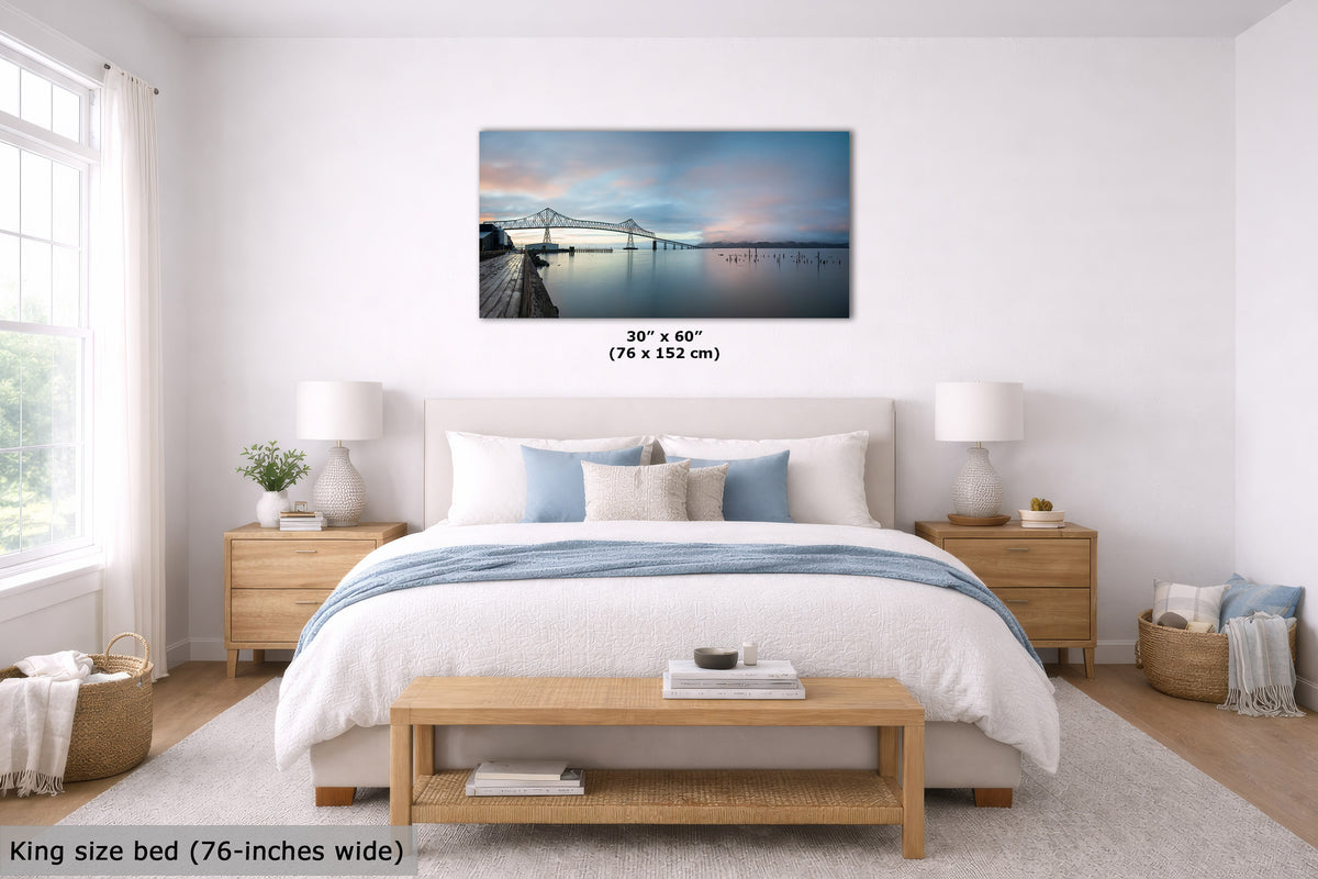 A framed wall art print showing a pier and bridge over calm water, displayed above a neatly made bed in a bright, modern bedroom. The print is labeled 30 x 60 inches (76 x 152 cm), and the room scene includes a bed, nightstands, lamps, and a bench.