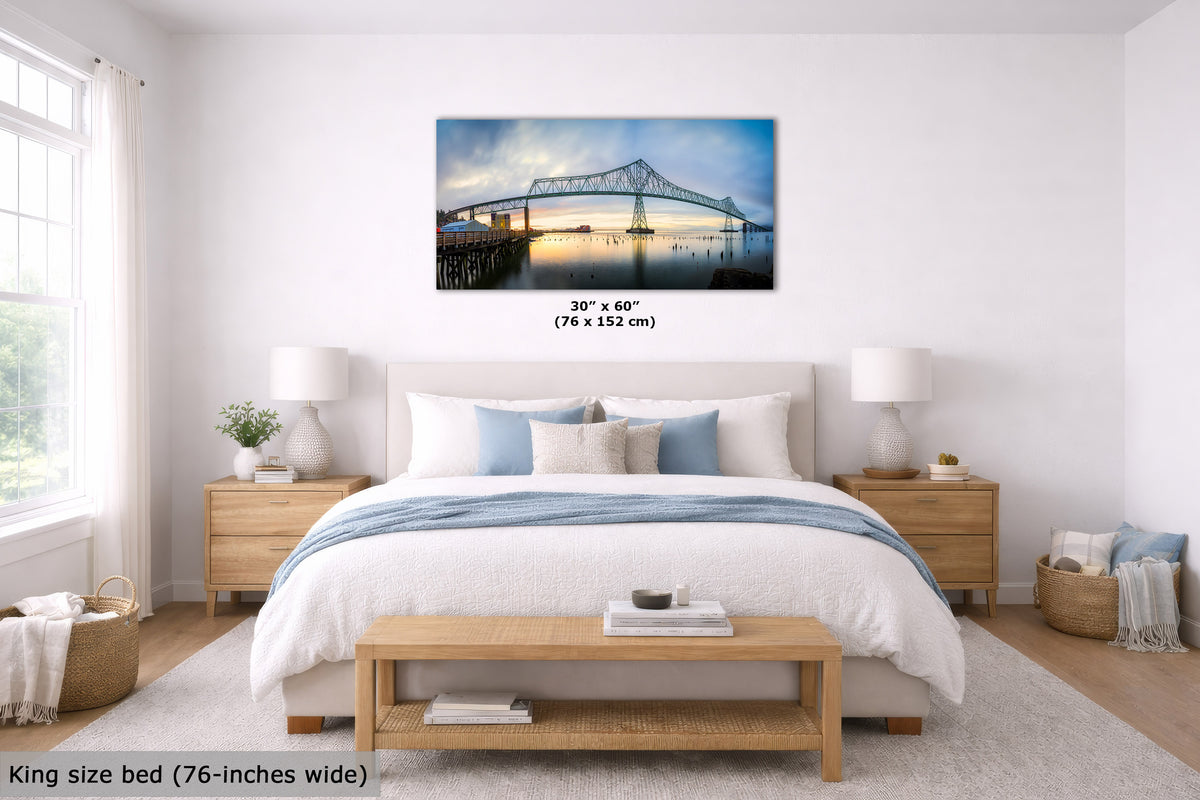 A framed wall art print showing a bridge over water, displayed above a neatly made bed in a bright, modern bedroom. The print includes size text reading 30" x 60" (76 x 152 cm), and the room scene includes a king size bed (76-inches wide) with bedding and bedside tables.