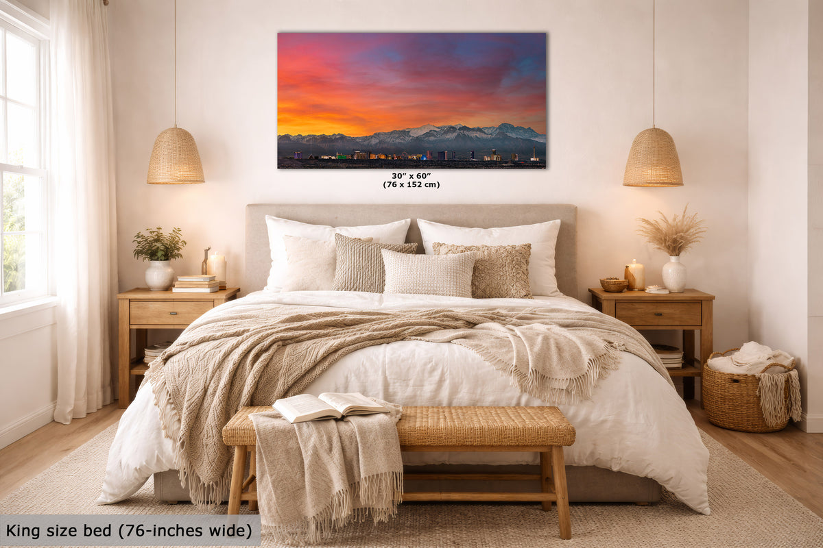 A framed wall art print showing a colorful mountain sunset hangs above a neatly made bed in a bright, modern bedroom. The print includes a size label reading 30 x 60 inches, and the room scene includes a text overlay noting the king size bed is 76-inches wide.