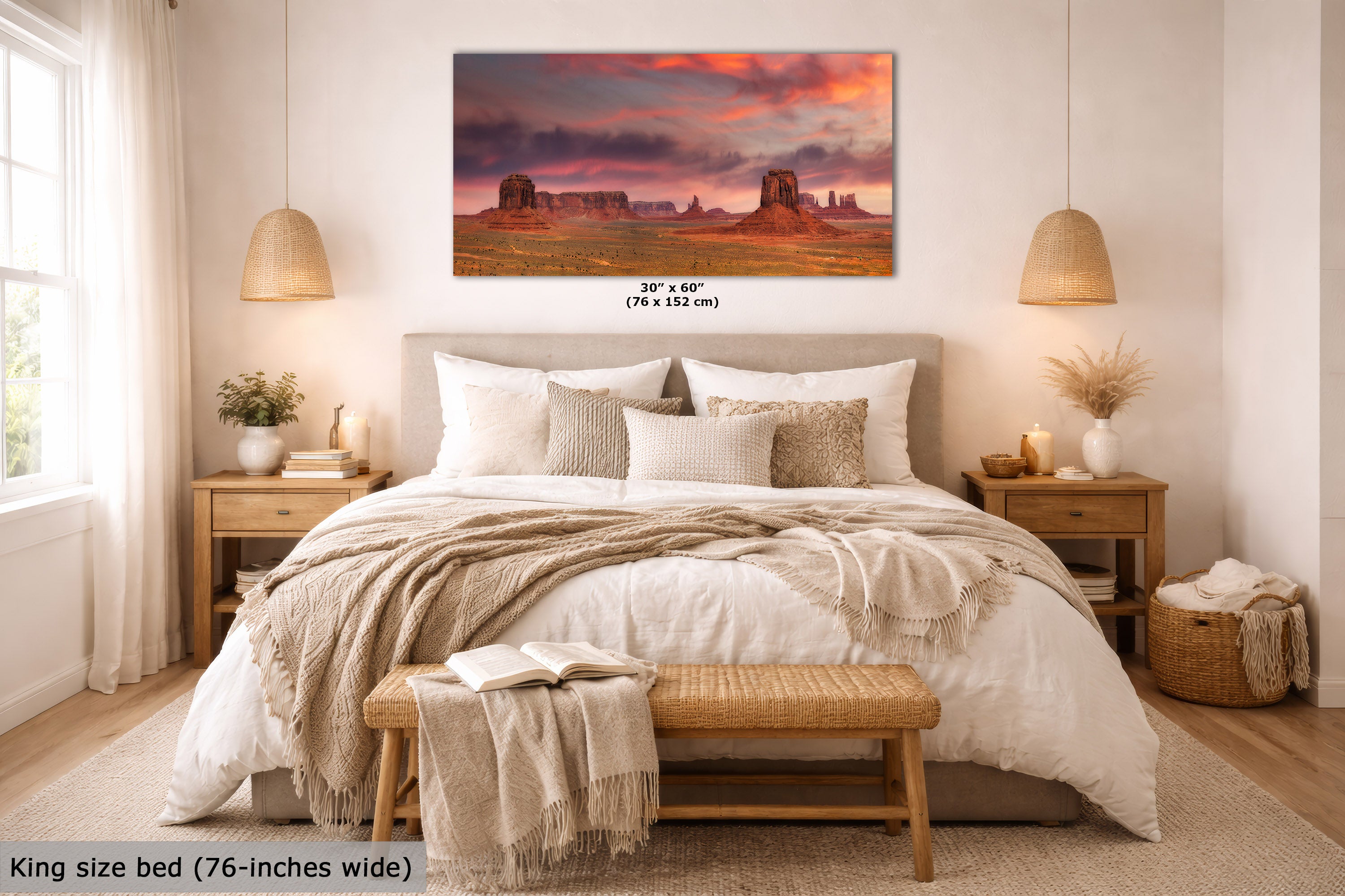 A wall art print depicting Monument Valley under a dramatic sunset sky is displayed above a neatly made bed in a styled bedroom. The print includes size text reading 30 x 60 inches (76 x 152 cm), and the room scene includes a king-size bed, bedside tables, lamps, and a bench.