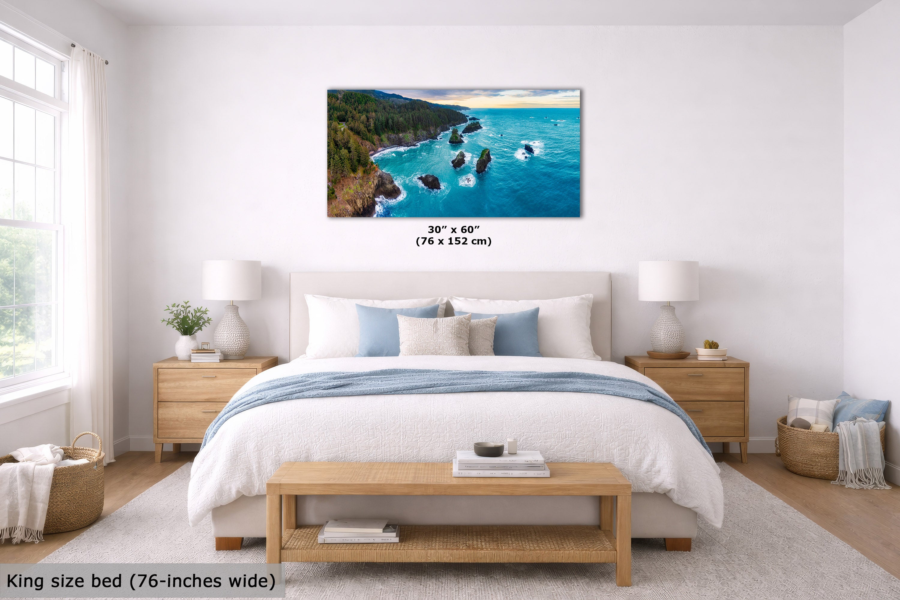 A coastal landscape wall art print displayed above a neatly made bed in a bright, modern bedroom. The print shows turquoise water, rocky shoreline, and green forest.