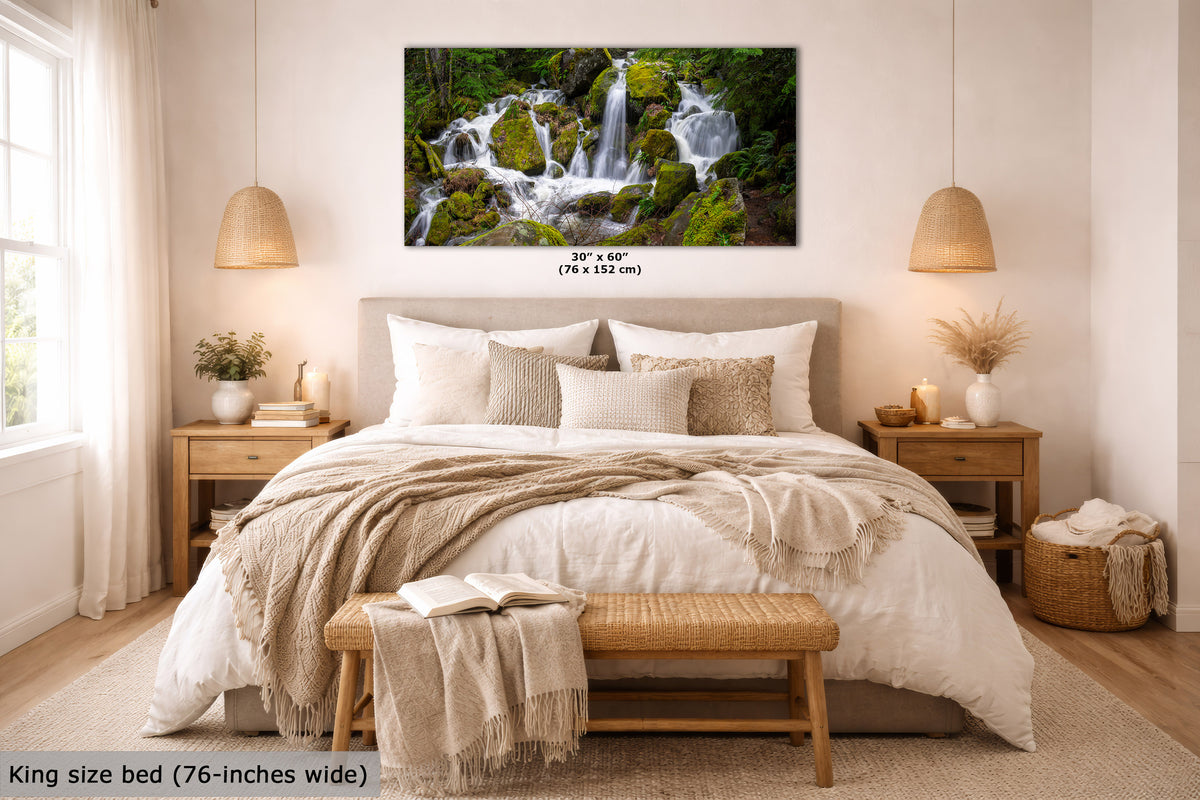 A framed wall art print showing a lush green forest waterfall, displayed above a neatly made bed in a bright, modern bedroom. The print includes size text indicating 30" x 60" (76 in x 152 cm).