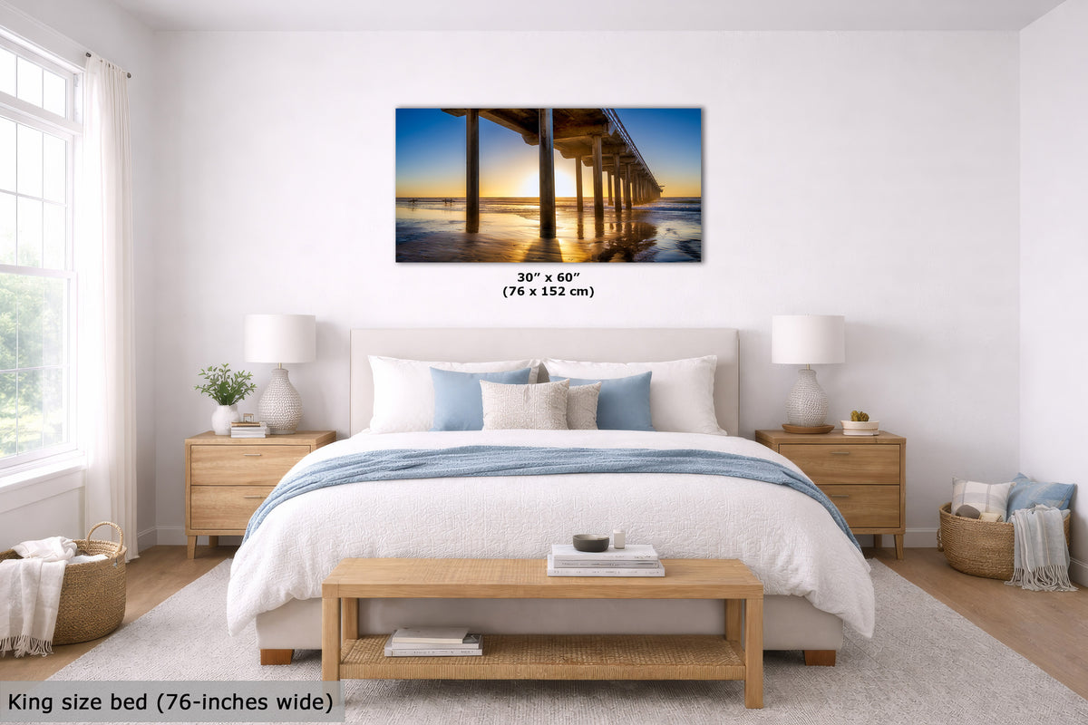 A wall art print showing a pier over water at sunset, displayed above a bed in a bright, modern bedroom. The print includes size text reading 30" x 60" (76 x 152 cm).
