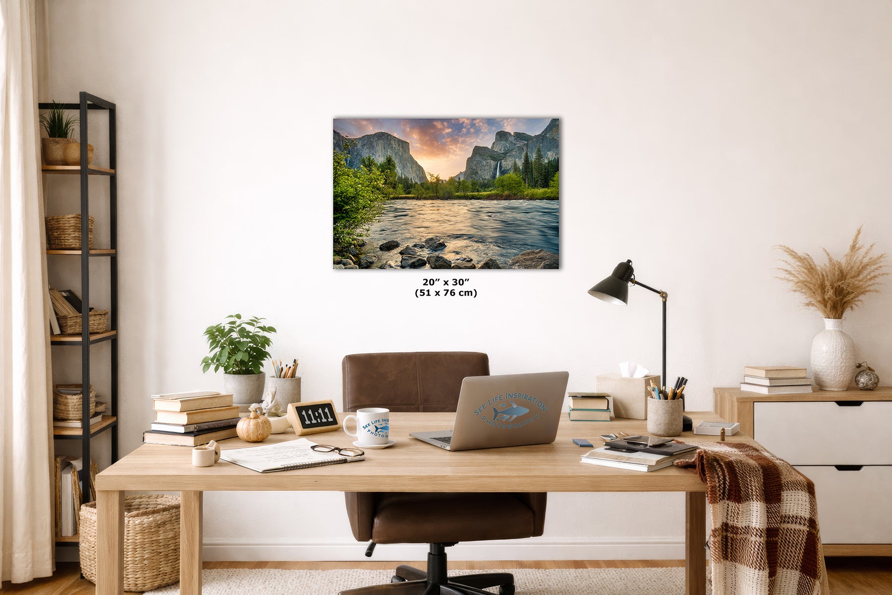 A framed wall art print of Yosemite's Valley View at sunrise, featuring El Capitan and the Merced River with Bridalveil Falls, displayed above a wooden desk in a styled home office interior. The print includes size text reading 20" x 30" (51 x 76 cm) below it.