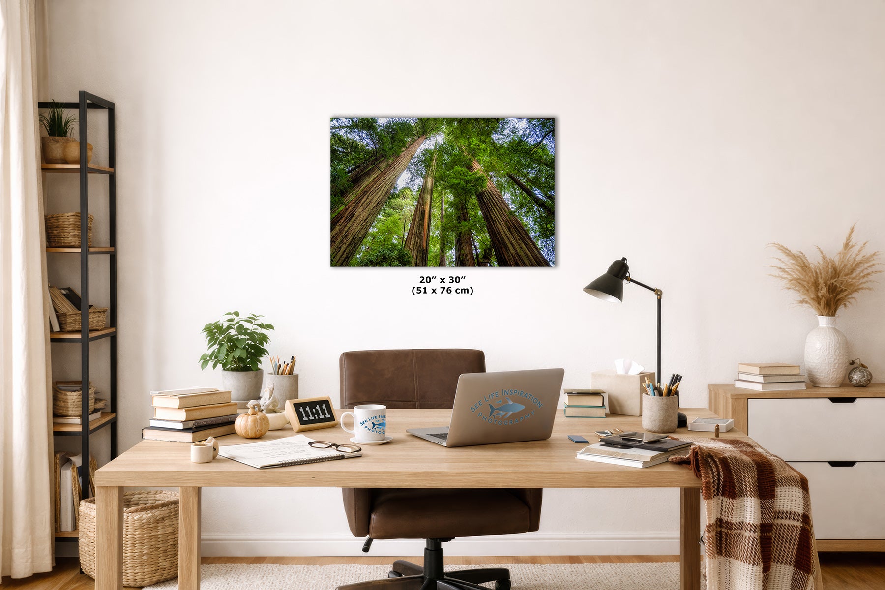 A wall art print depicting a forest of tall redwood trees, displayed in a styled home office setting above a wooden desk with a laptop, lamp, and other office accessories.