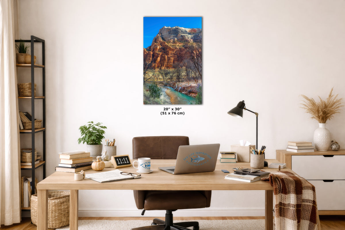 A wall art print showing a colorful canyon landscape with a river, displayed above a wooden desk in a styled home office setting. The print includes size text indicating 20 x 30 inches.