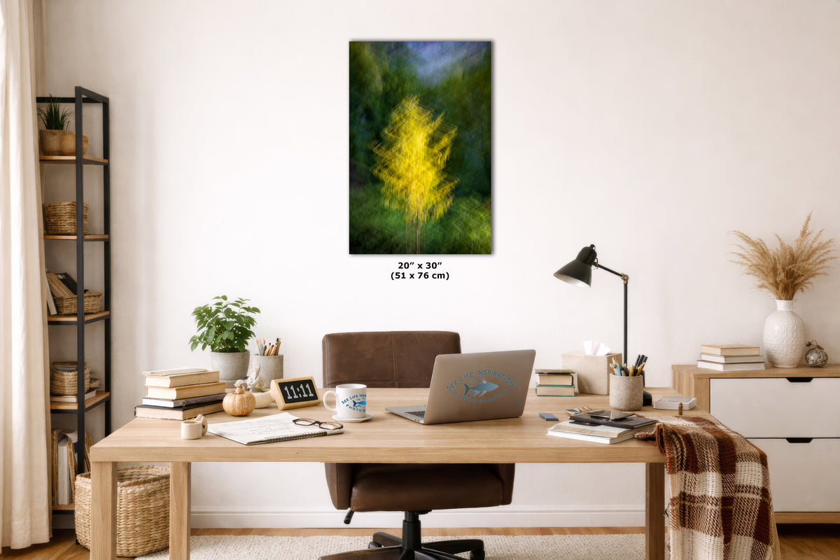 A framed wall art print showing a bright yellow tree in a green forest, displayed above a wooden desk in a modern home office setting. The print has a size label printed below it reading 20 x 30 inches.