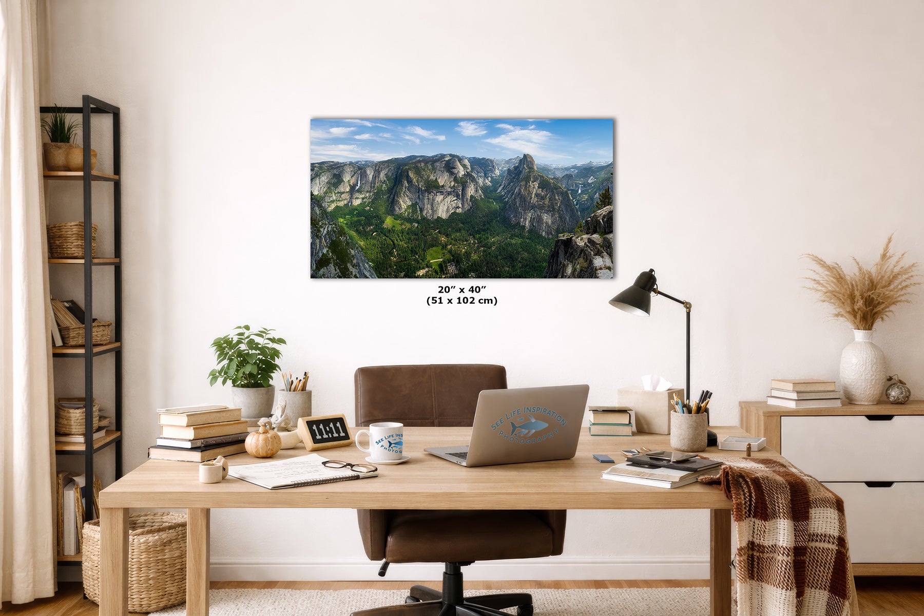 A rectangular wall art print showing Yosemite Valley and Half Dome from Glacier Point with green valleys and blue sky, displayed above a wooden desk in a styled home office. The print includes size text reading 20" x 40" (51 x 102 cm).