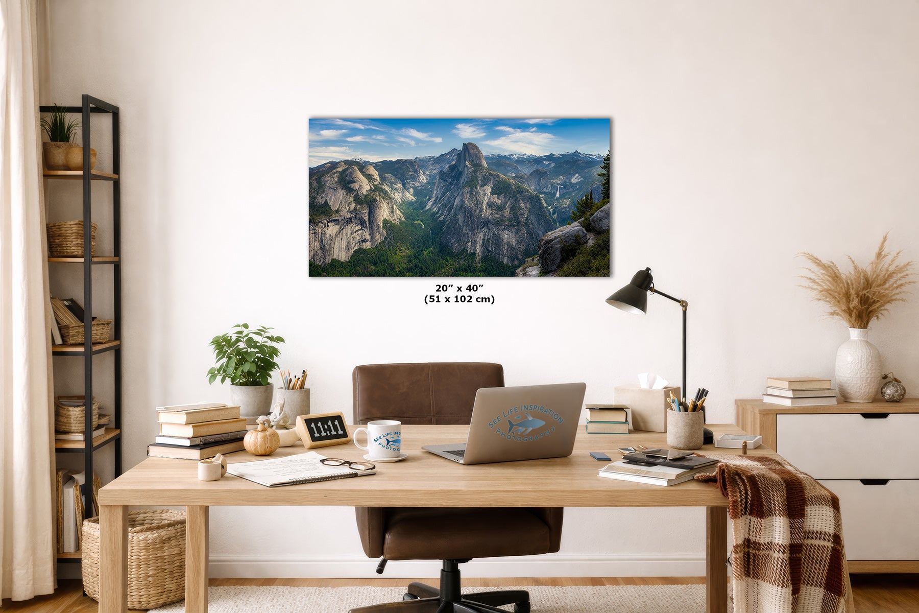 A rectangular wall art print showing a Yosemite mountain landscape with blue sky and green slopes, displayed above a wooden desk in a styled home office. The print includes size text reading 20 x 40 in (51 x 102 cm).
