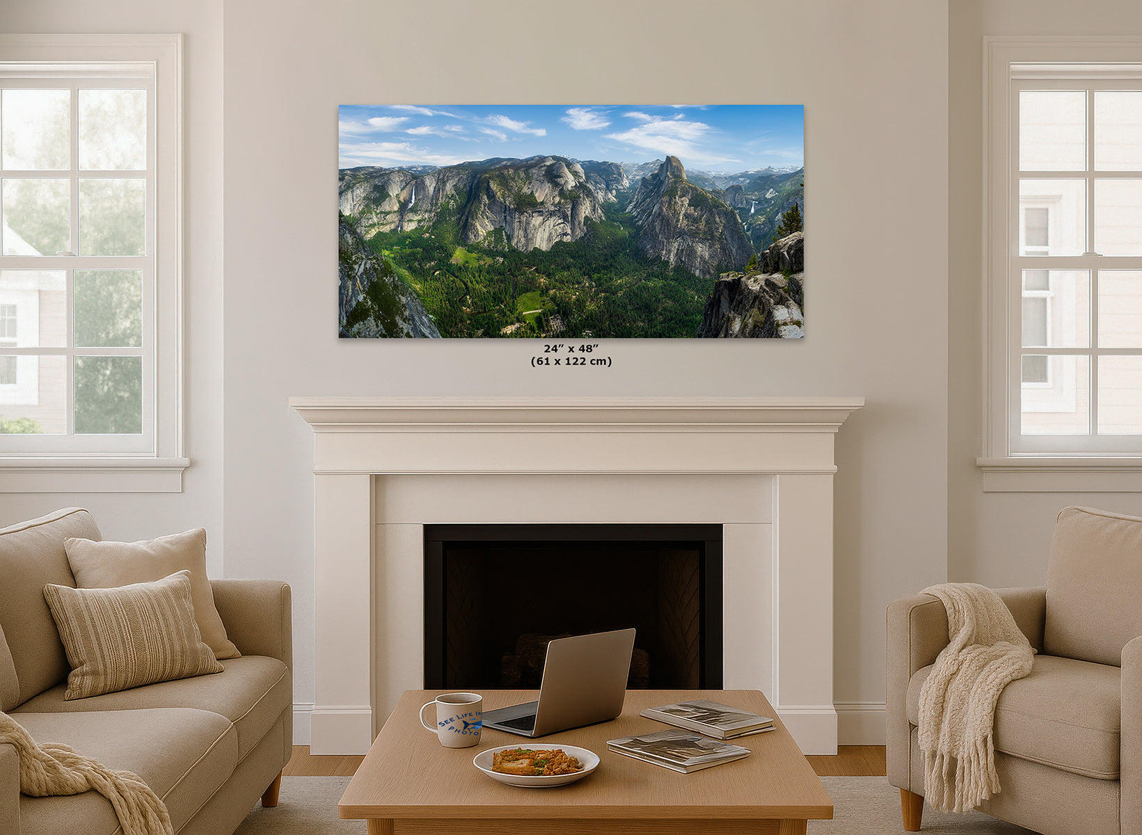 A framed wall art print showing Yosemite Valley and Half Dome from Glacier Point, a mountain valley landscape, hangs above a white fireplace in a bright living room. The print includes the text '(24 x 48 in)'.