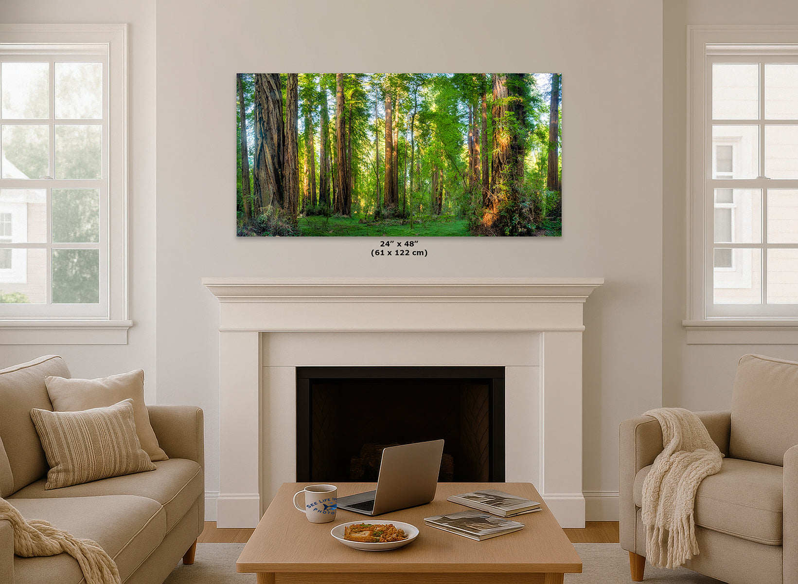 A California Redwood forest wall art print hangs above a white fireplace mantel in a bright living room with beige sofas, a coffee table, and windows on both sides. The print depicts tall green trees with warm sunlight filtering through the canopy.