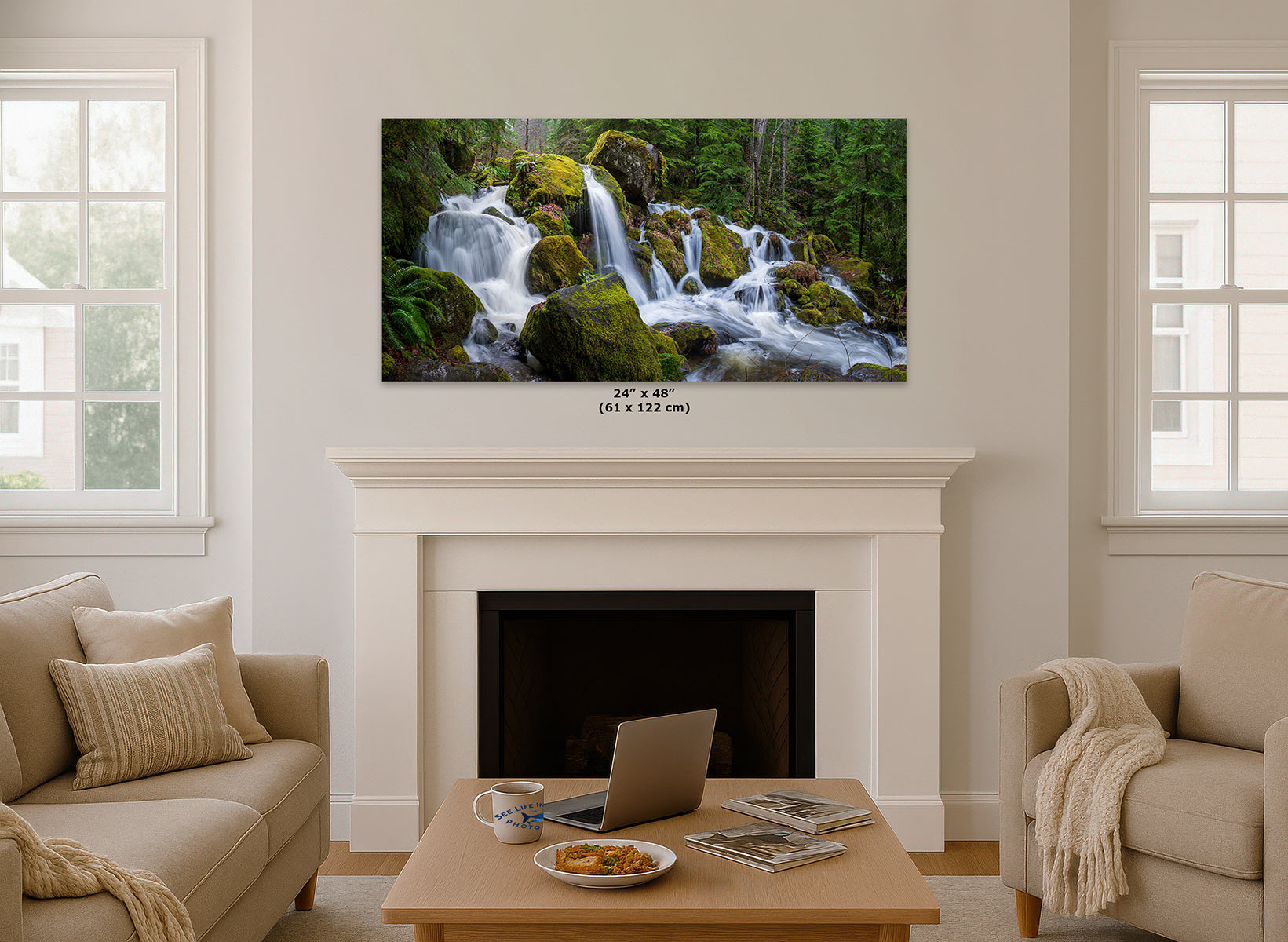 A framed wall art print showing a lush green forest waterfall, displayed above a white fireplace mantel in a modern living room setting with beige sofas and a wooden coffee table.