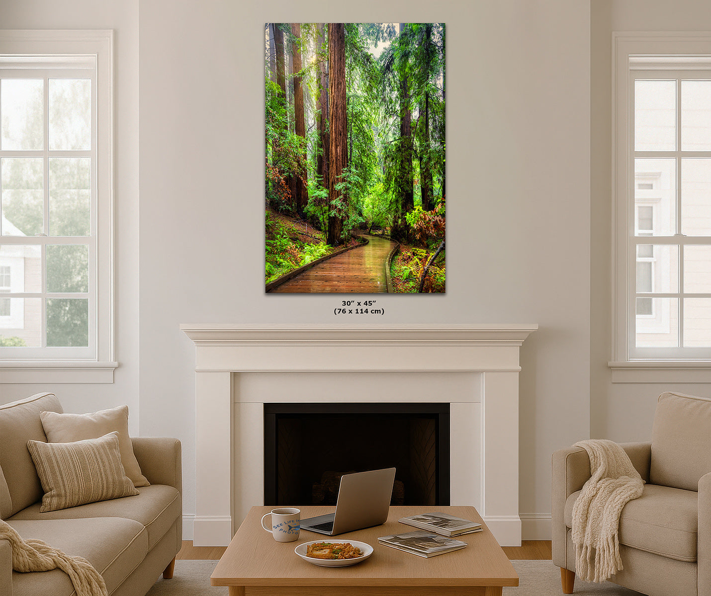 A vertical canvas wall art print depicting a lush green forest path with tall Redwood trees, displayed above a white fireplace mantel in a modern living room setting with beige sofas and a wooden coffee table.
