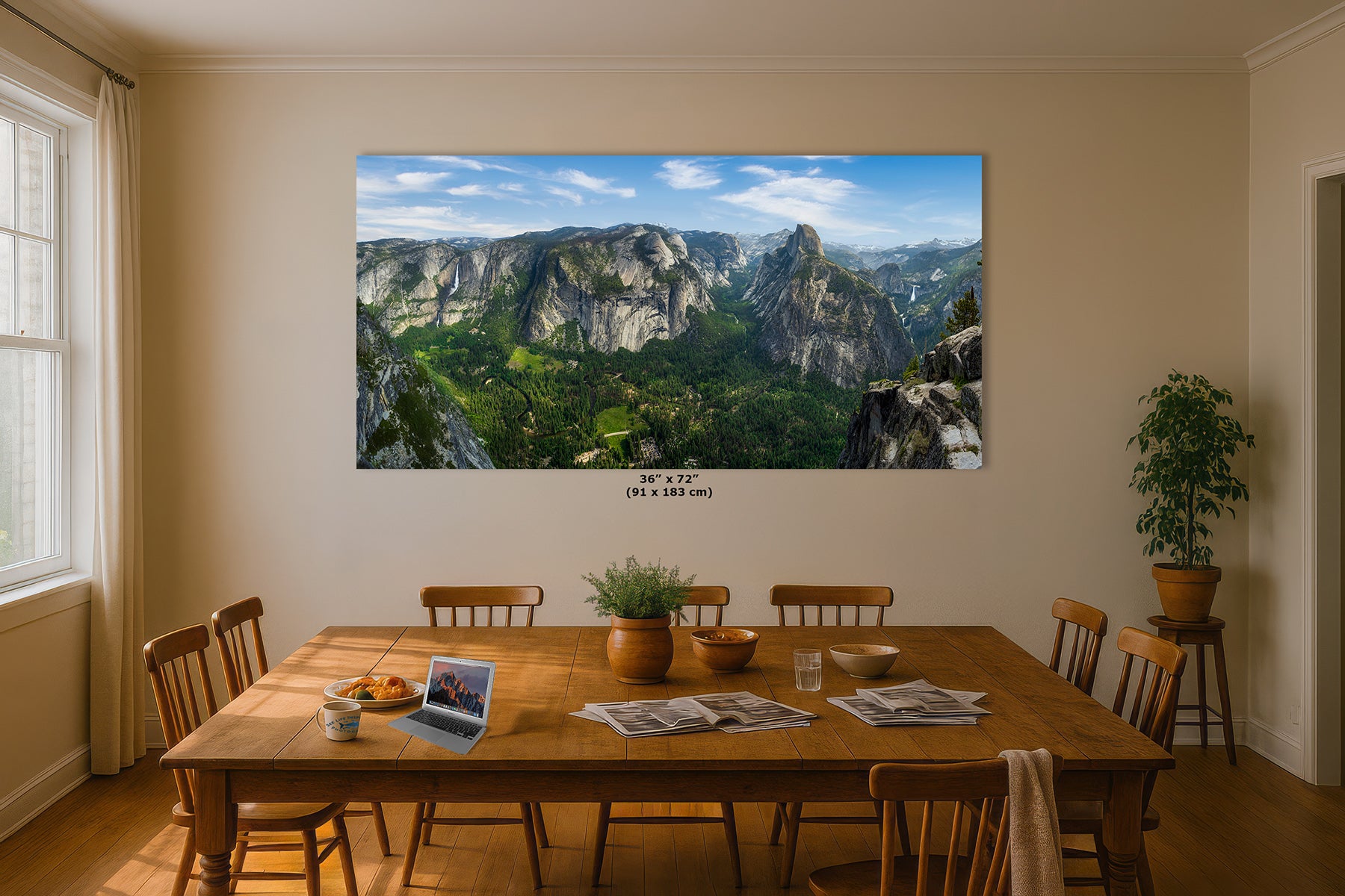 A large landscape wall art print showing Yosemite Valley and Half Dome from Glacier Point, a mountain valley with green forests and blue sky, displayed above a wooden dining table in a warm, modern dining room. The print includes size text reading 36 x 72-inches.