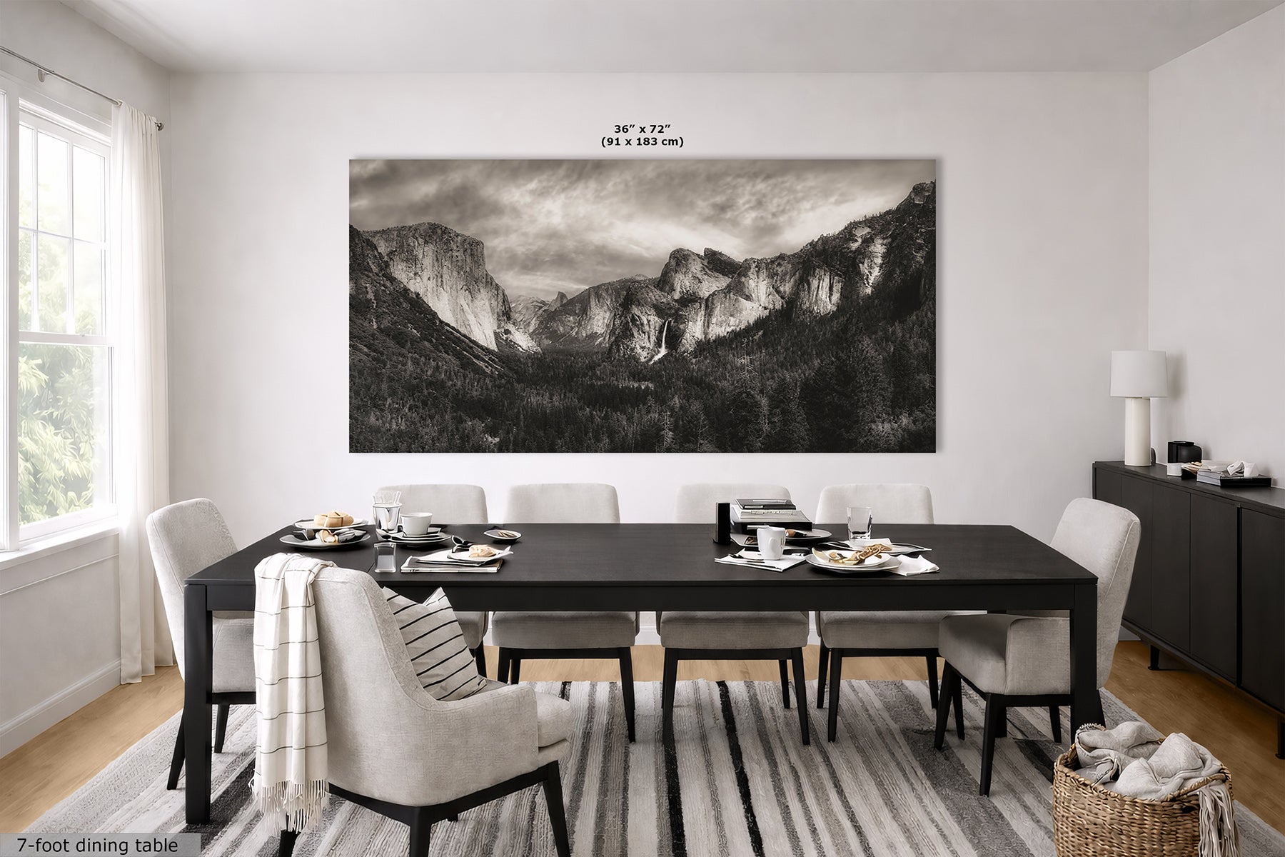 A large black-and-white landscape print of Yosemite Valley hangs on a white wall above a dark wood dining table and light upholstered chairs in a modern dining room.