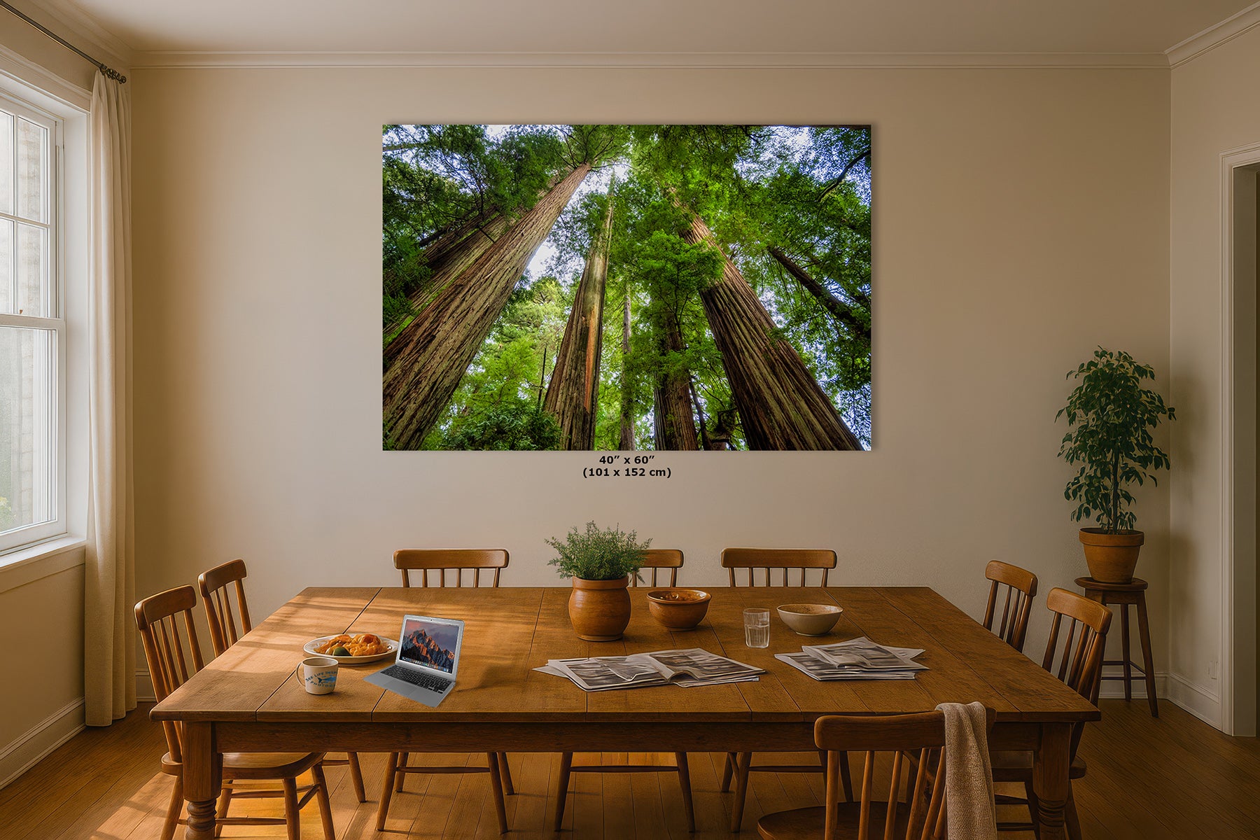 A large framed wall art print depicting a low-angle view looking up through tall redwood trees is displayed on a beige wall in a dining room with a wooden table and chairs.