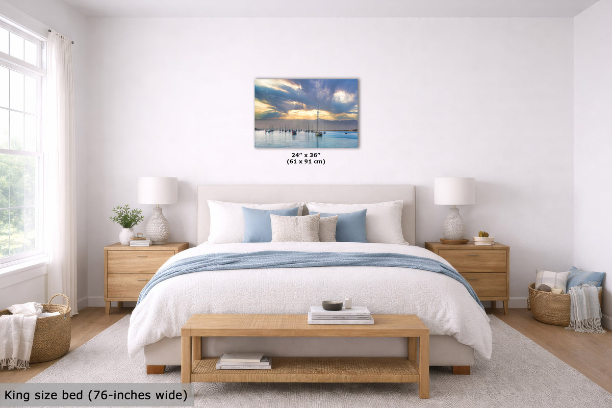A wall art print showing a scenic sunrise over calm water with a sailboat, displayed above a neatly made bed in a bright, modern bedroom. The print includes size text reading 24" x 36" (61 x 91 cm).