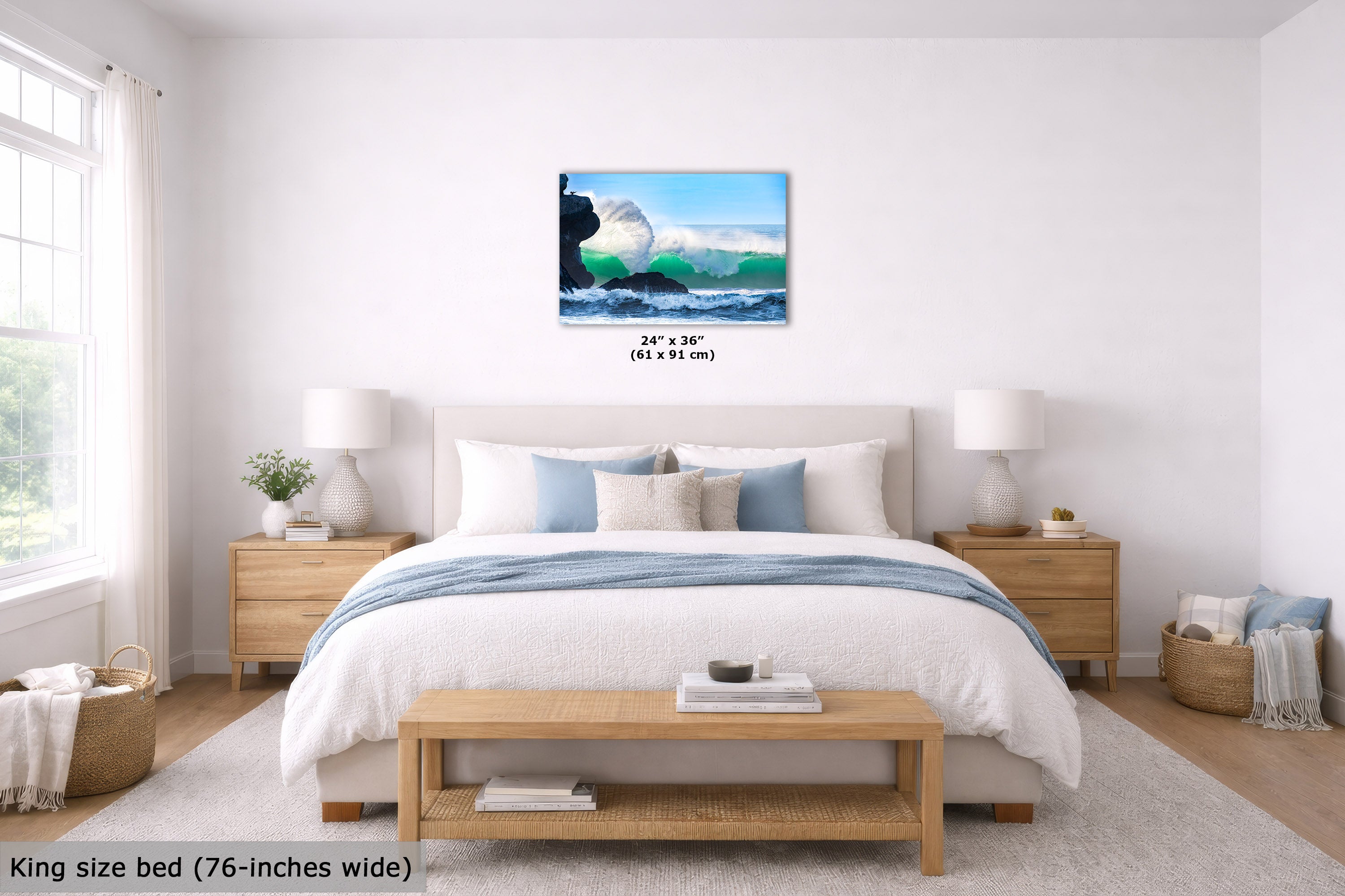 An ocean wave canvas print displayed on a white wall above a neatly made bed in a bright, modern bedroom. The print shows a white surf wave crashing against dark rocks under a blue sky.