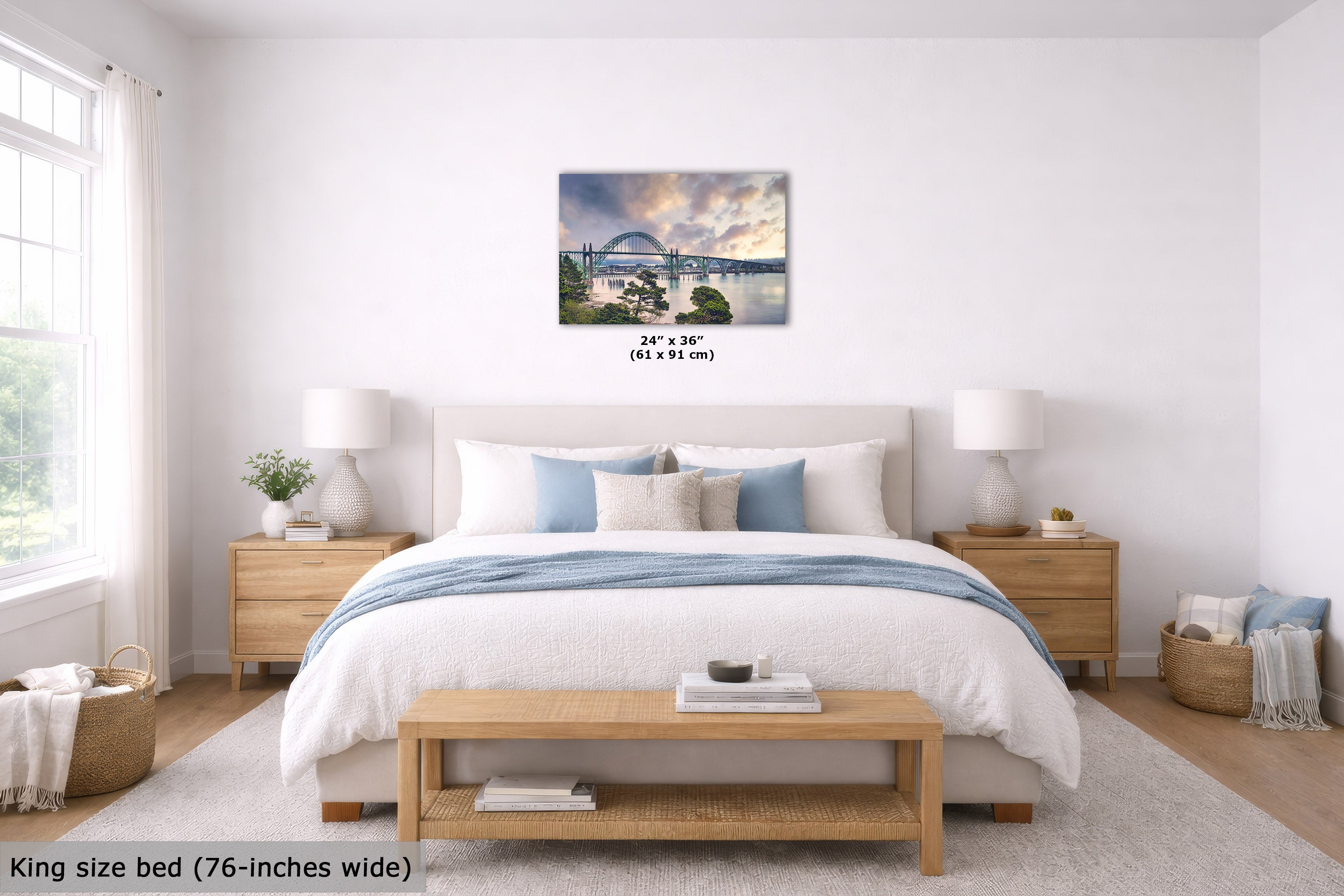 A wall art print depicting a scenic bridge over water under a dramatic cloudy sky, displayed above a neatly made bed in a bright, modern bedroom. The print includes size text reading 24" x 36" (61 x 91 cm).