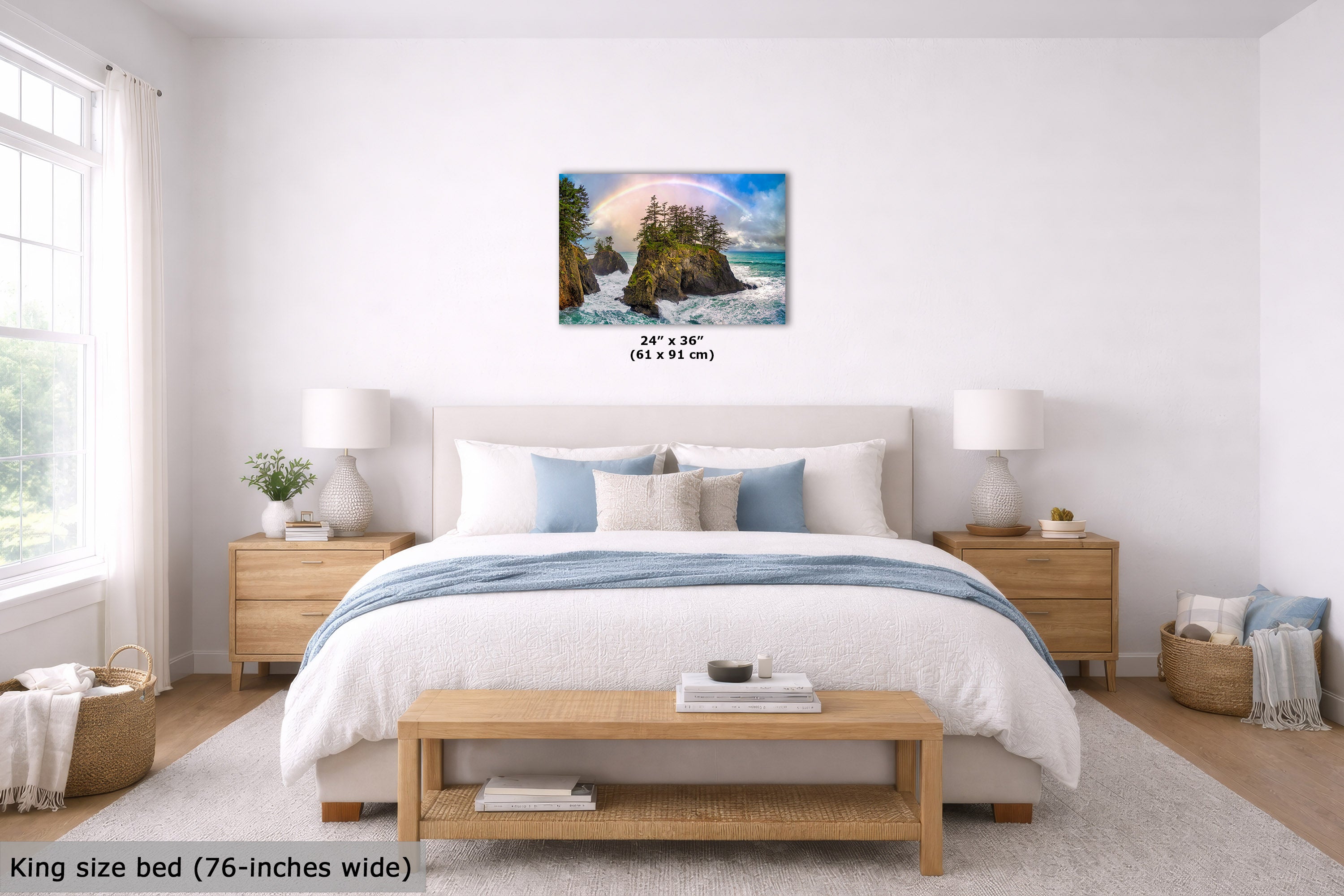 A wall art print showing a coastal rocky shoreline with turquoise water and a rainbow, displayed above a neatly made bed in a bright, modern bedroom. Small text below the artwork reads 24" x 36" (61 x 91 cm).