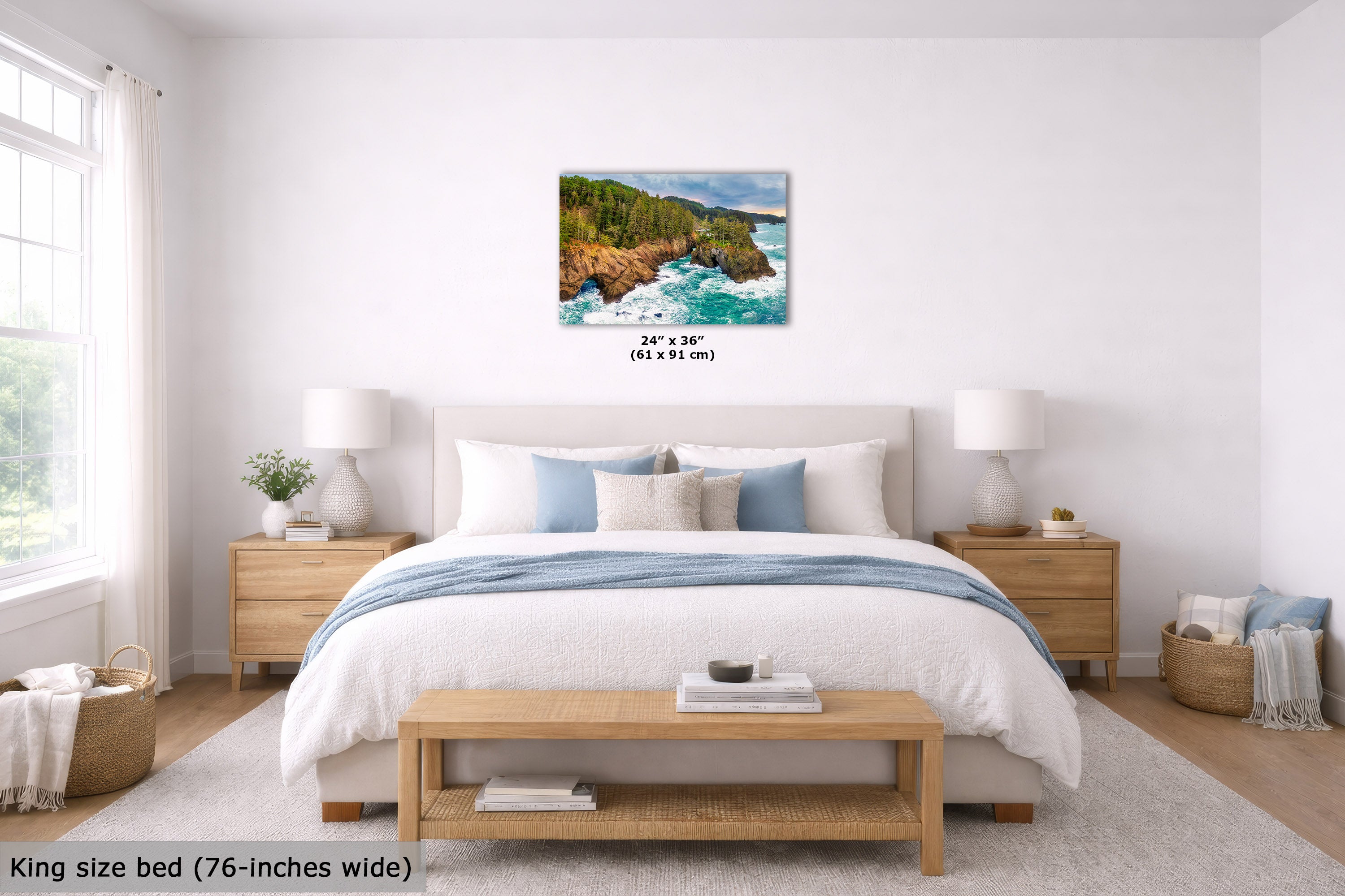 A coastal landscape wall art print hangs above a neatly made bed in a bright, modern bedroom. The print shows green cliffs and blue ocean water.