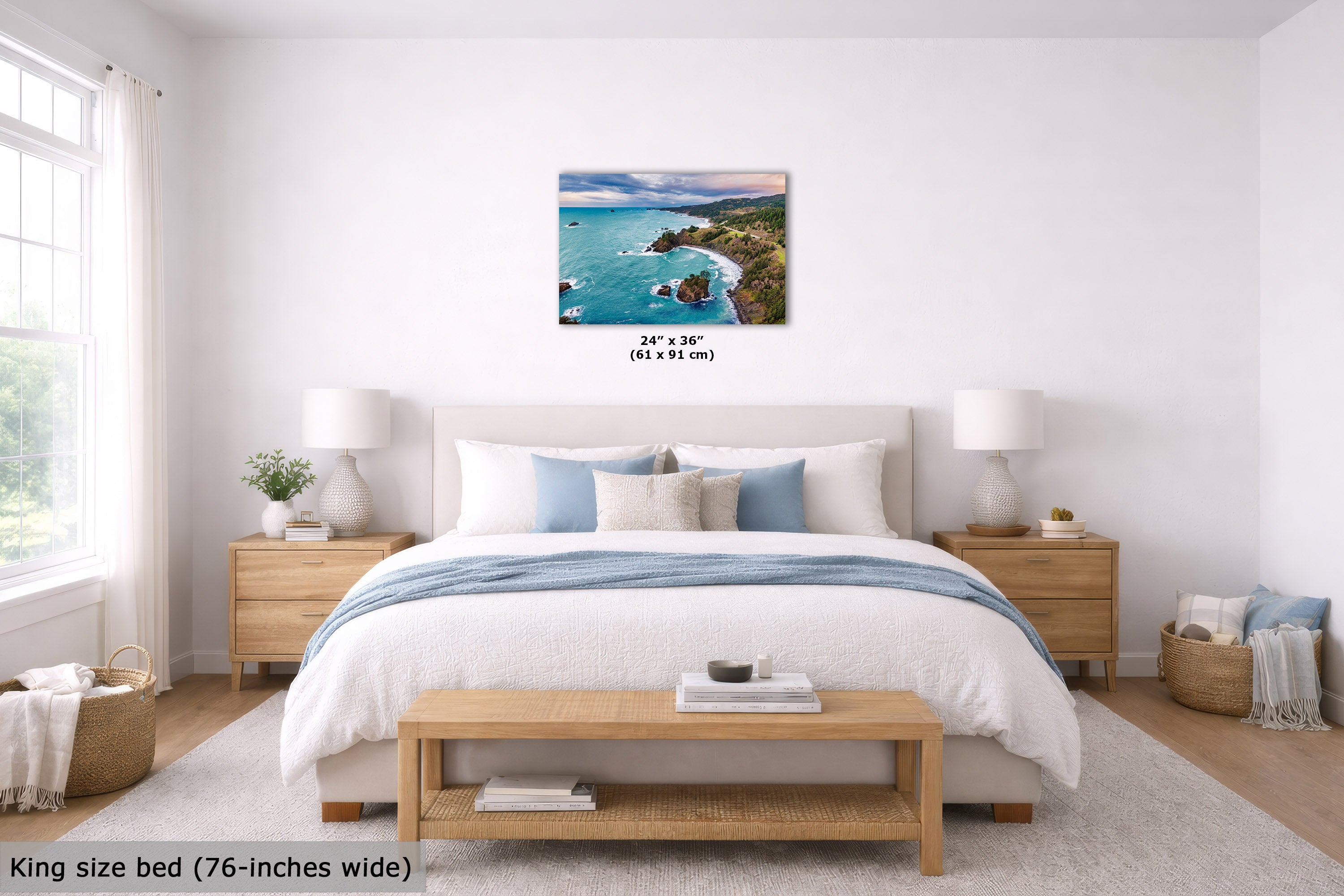 A coastal landscape wall art print hangs above a neatly made bed in a bright, modern bedroom. The print shows turquoise water, rocky shoreline, and green cliffs.