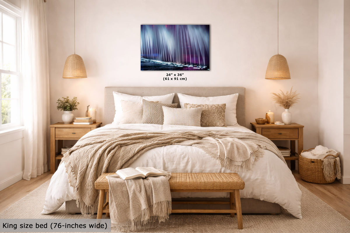 A bedroom scene showing a wall art print above a bed. The product appears to be the wall art itself, depicting a moody water fountain show in blue, purple, and white tones.