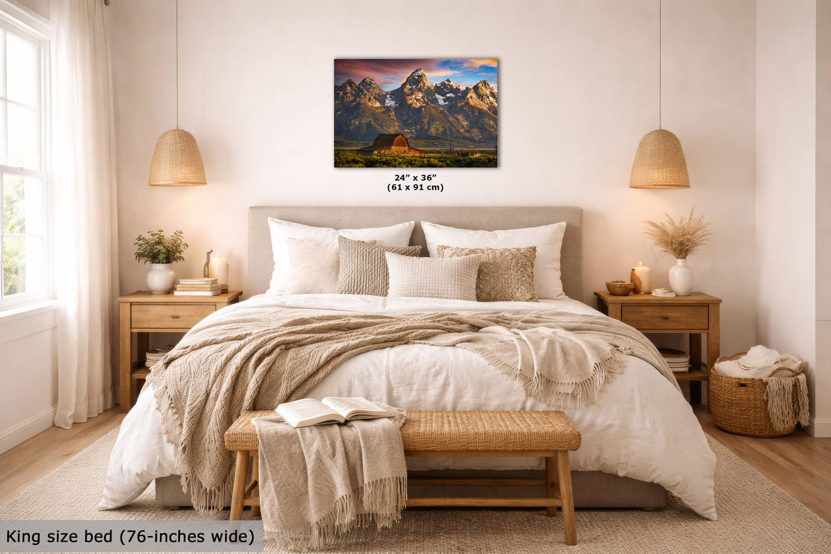 A mountain landscape wall art print is displayed above a neatly made bed in a bright, modern bedroom. The print shows snow-capped mountains under a colorful sky, with size text below it reading 24" x 36" (61 x 91 cm).