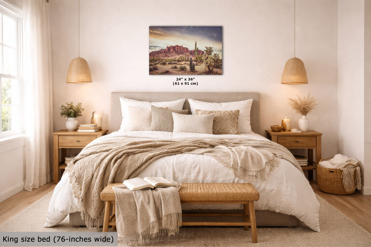 A desert landscape wall art print is displayed above a neatly made bed in a warm, modern bedroom. The print shows a desert scene with red rock formations and cacti under a cloudy sky.