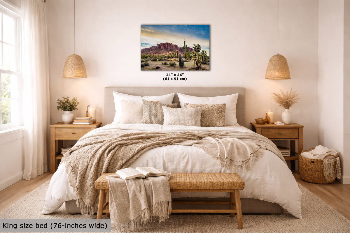A wall art print showing a desert landscape with cacti and a cowboy silhouette under a blue sky, displayed above a neatly made bed in a warm, modern bedroom. The print includes size text reading 24 x 36 inches (61 x 91 cm).