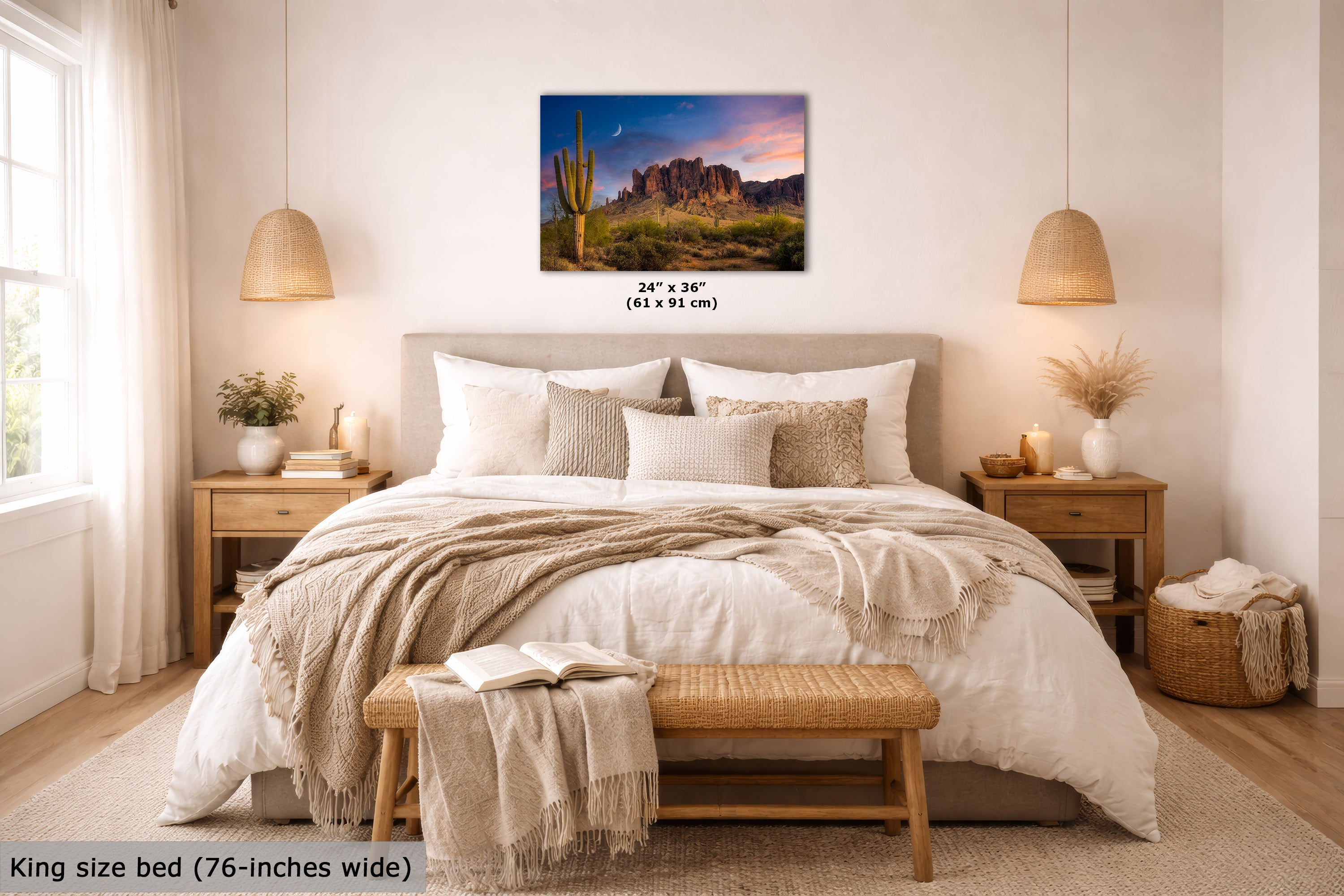 A wall art print showing a desert mountain landscape with cacti and a colorful sunset sky, displayed above a neatly made bed in a bright, modern bedroom. The print includes size text reading 24 x 36" (61 x 91 cm), and the image also notes the bed is king size (76-inches wide).